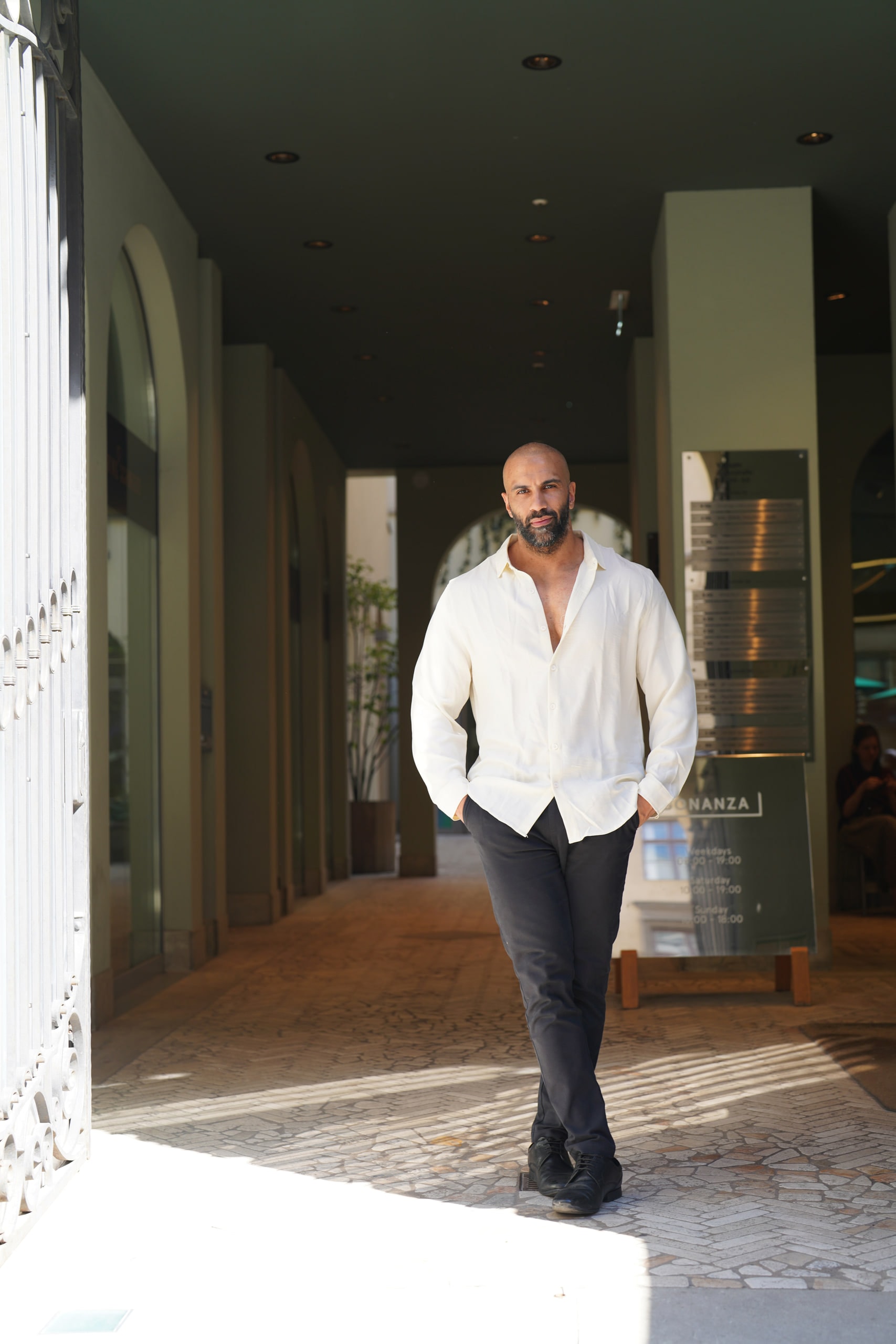 Amer El-Erwadi walking out of a shaded arcade into sunlight.