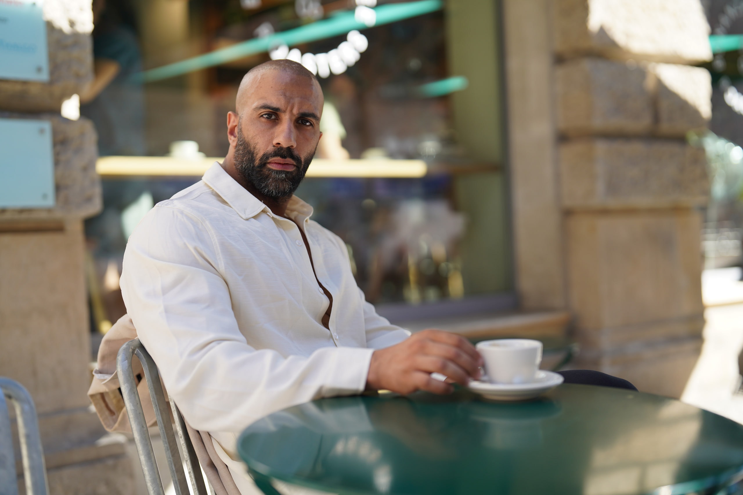 Amer El-Erwadi seated at a café table with an espresso, looking directly at the camera.
