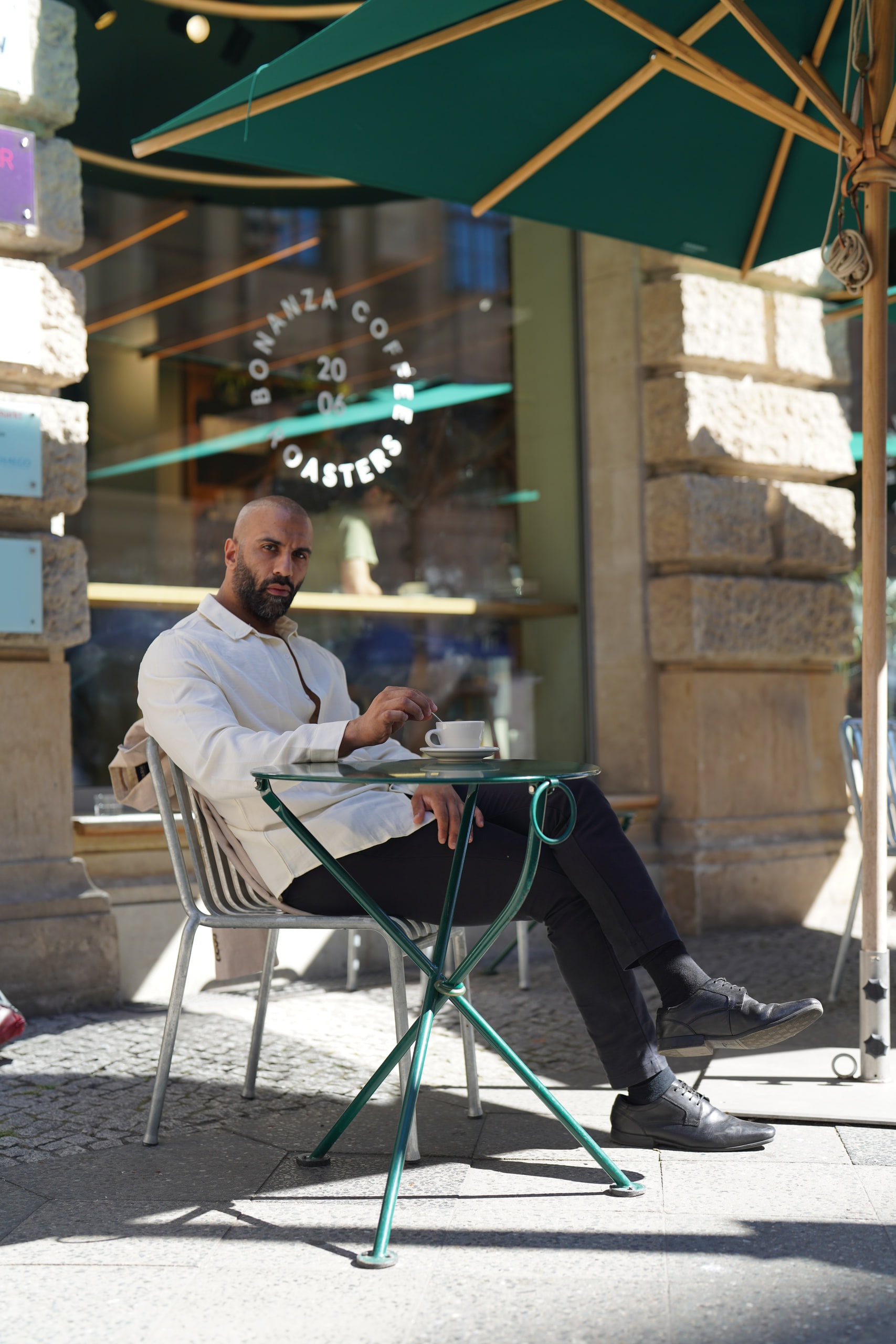 Amer El-Erwadi at a café terrace beneath a green parasol, legs crossed.