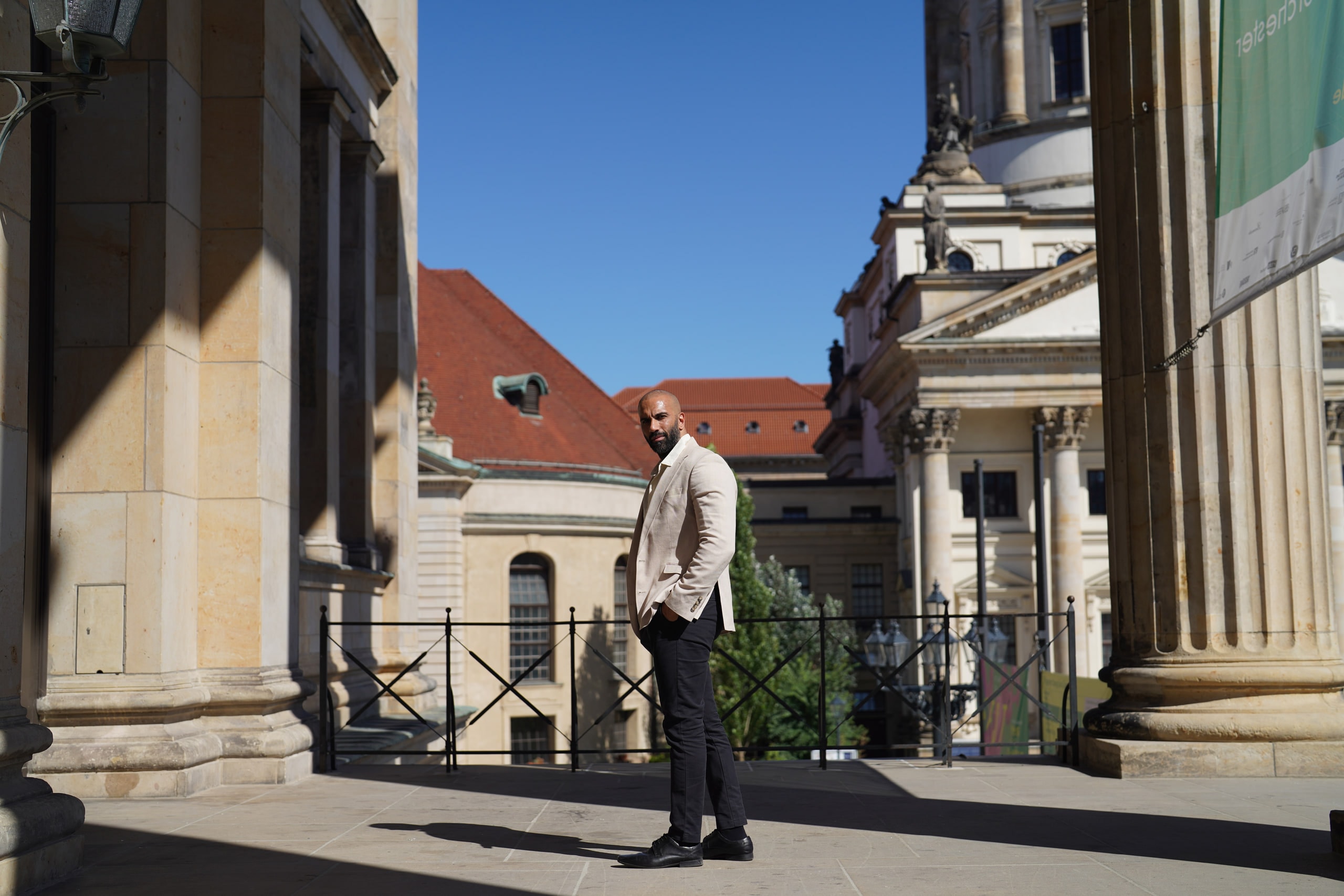 Amer El-Erwadi standing between columns, the Französischer Dom rising behind him.