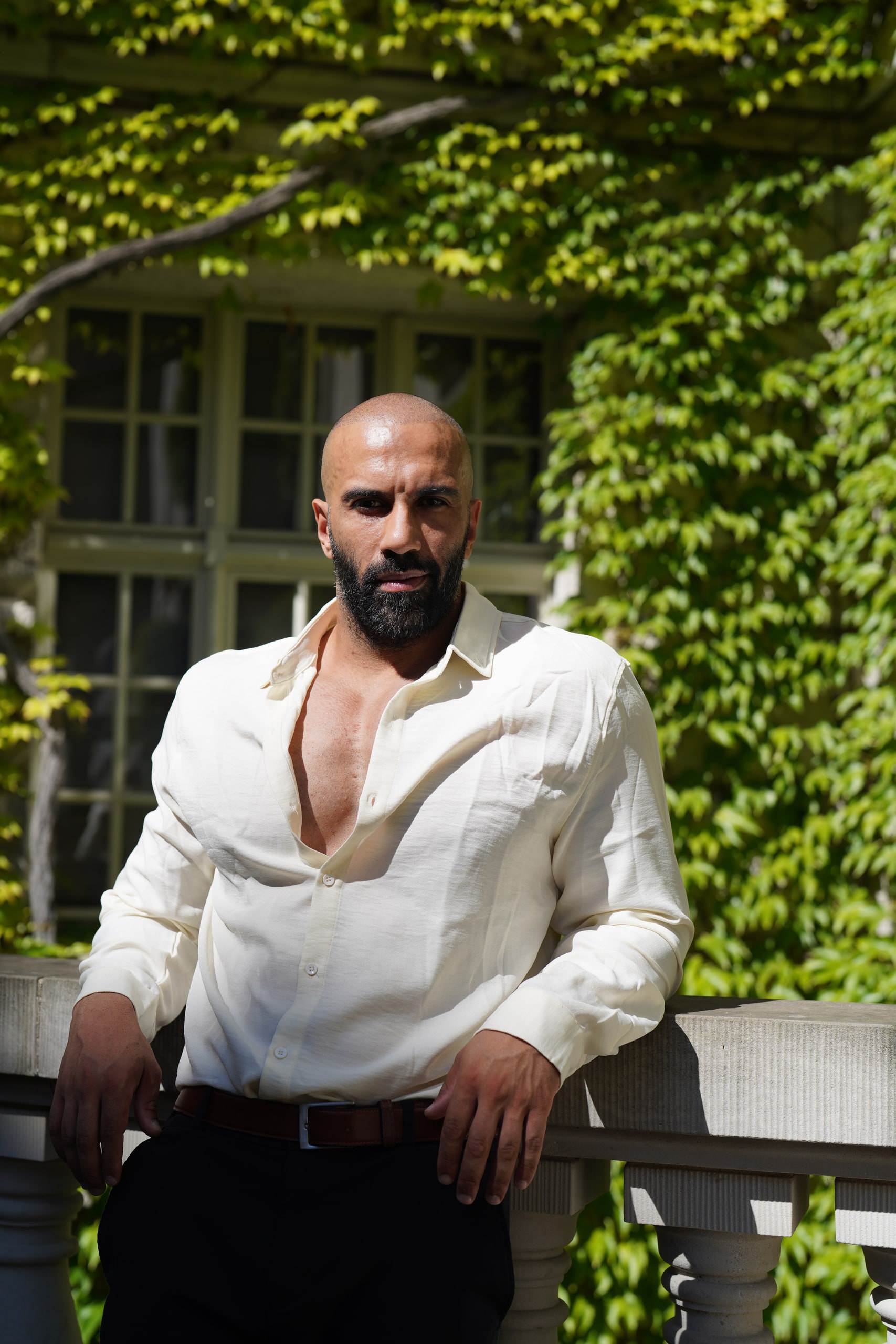 Amer El-Erwadi leaning against a stone balustrade with ivy behind him.