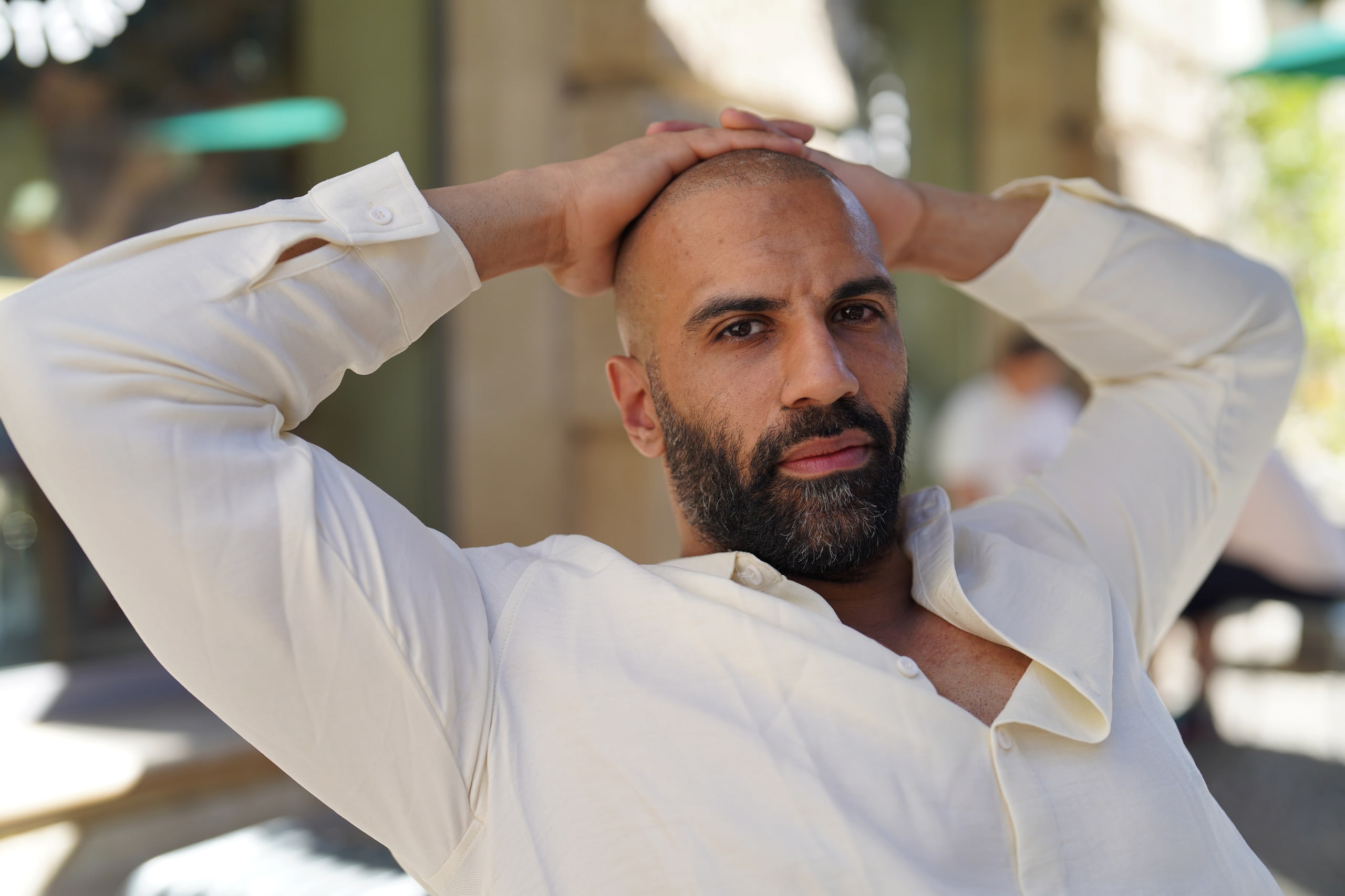 Close portrait of Amer El-Erwadi seated outdoors with his hands resting on his head, wearing a white shirt.