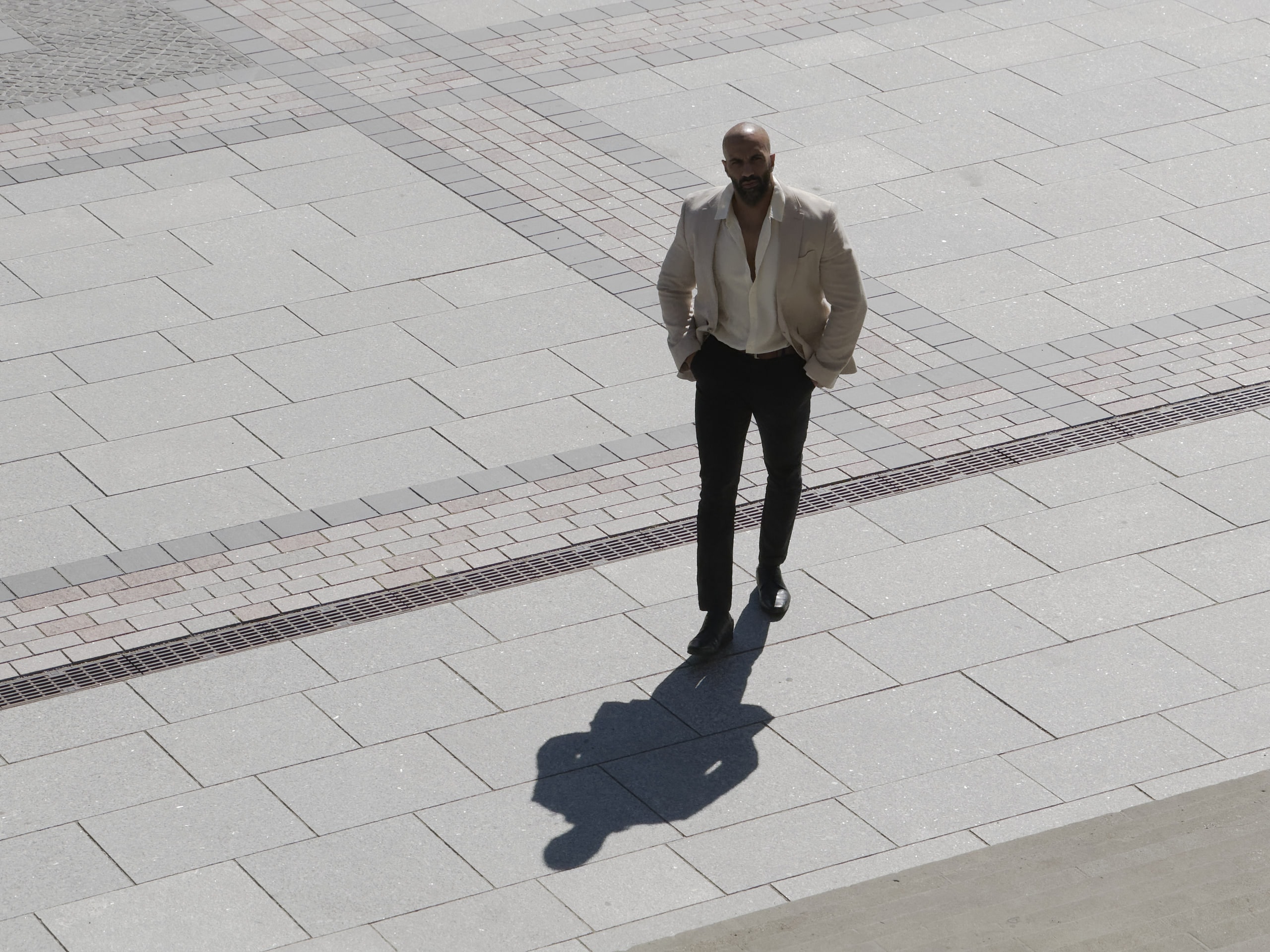 Amer El-Erwadi seen from above on the paving of Gendarmenmarkt, looking up with a long shadow stretching in front of him.
