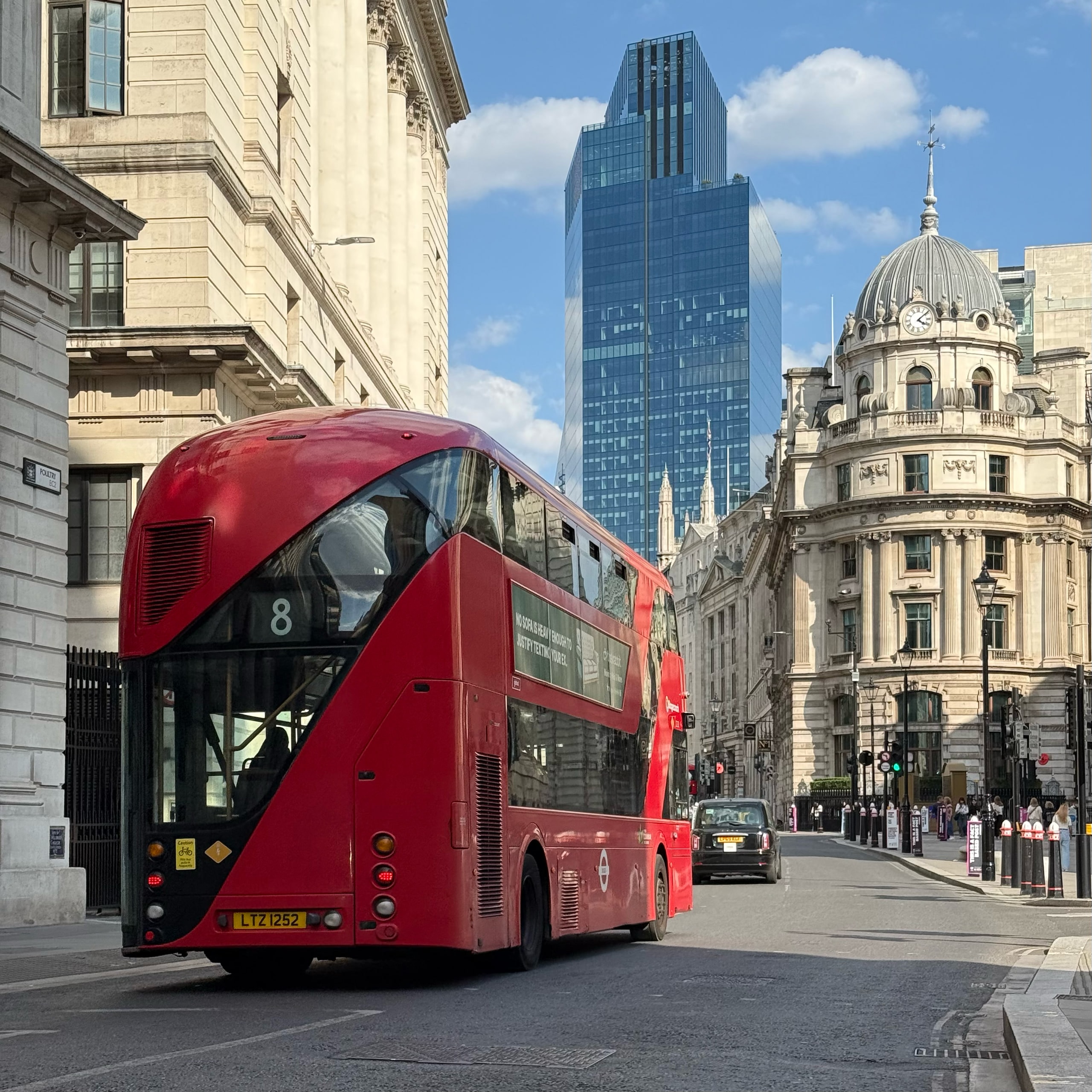 A red bus passing between a glass tower and a classical dome.