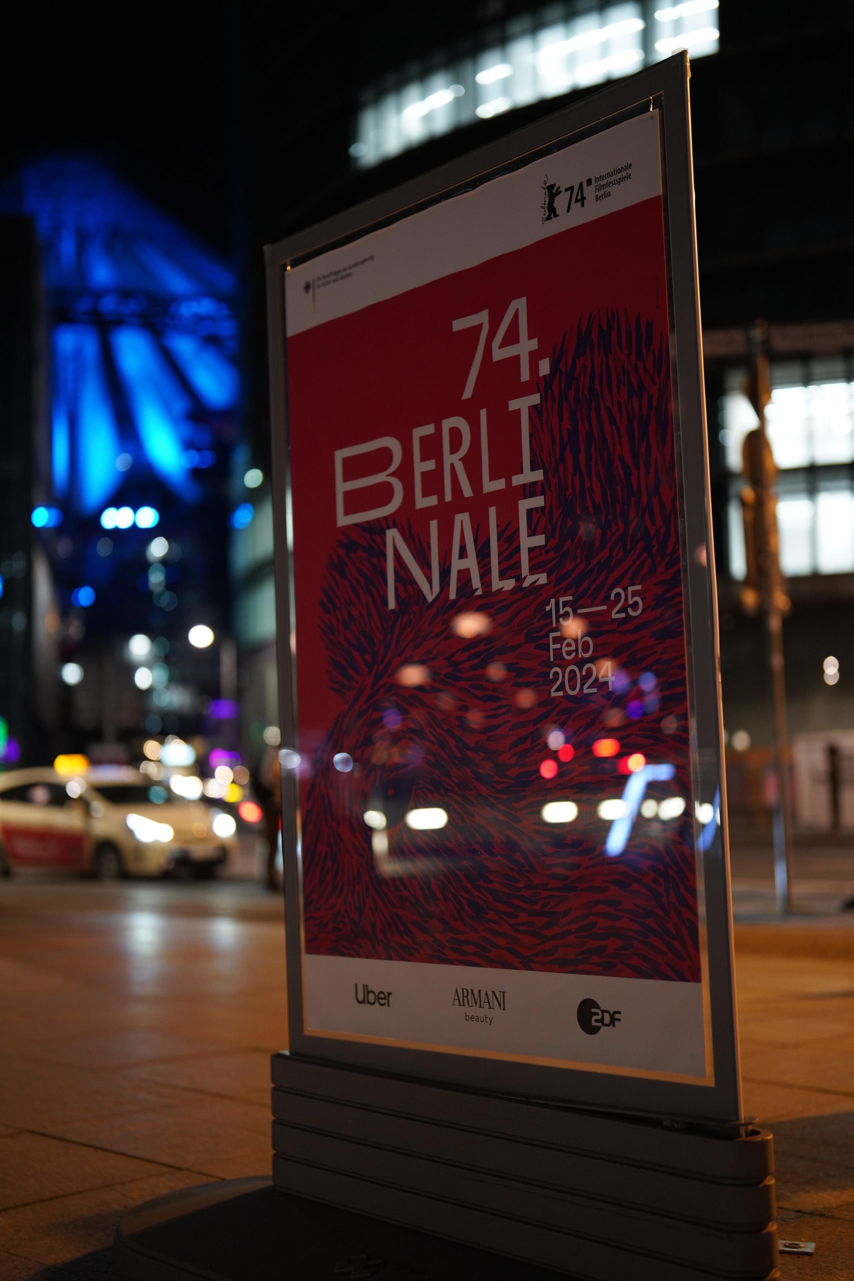 The 74th Berlinale poster lit on a street stand at night, traffic behind it.