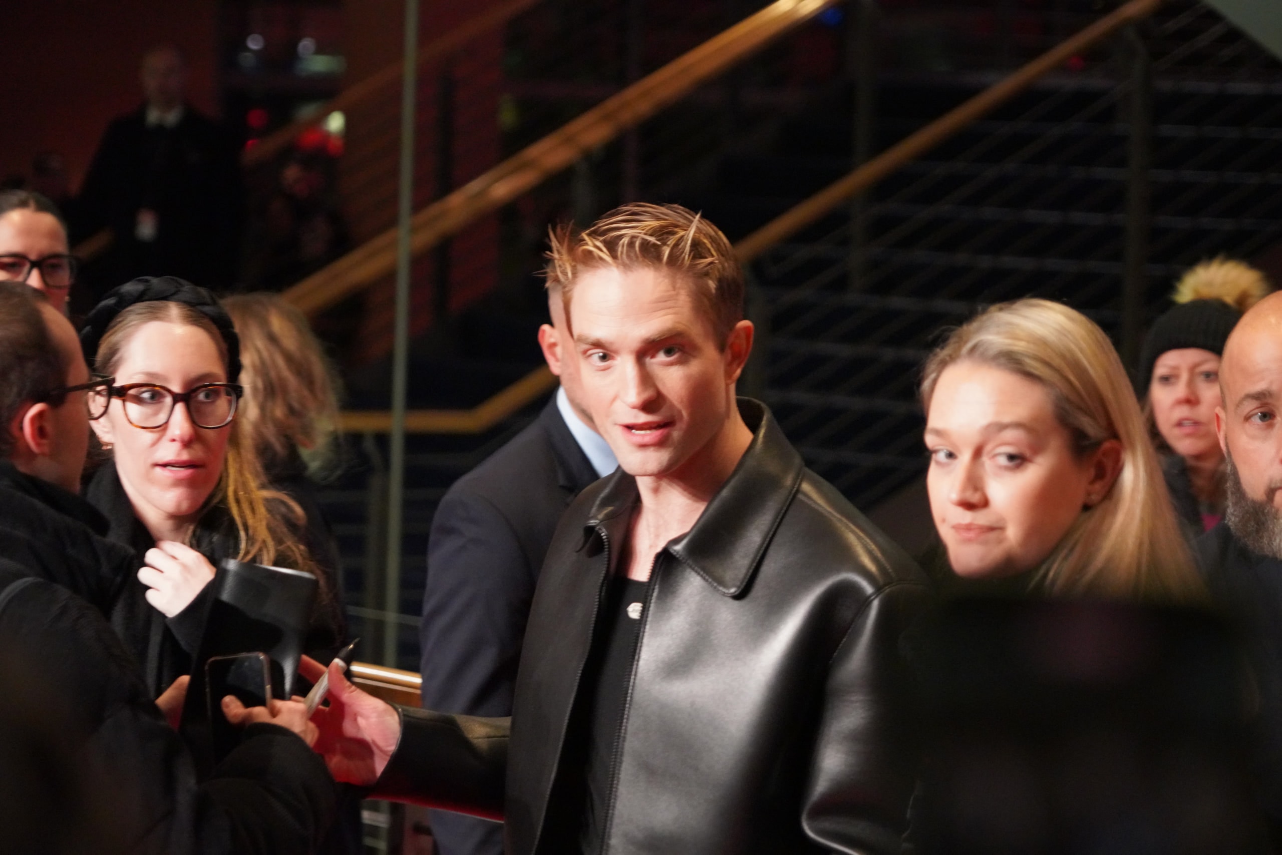 Robert Pattinson in a black leather jacket among the crowd on the red carpet.