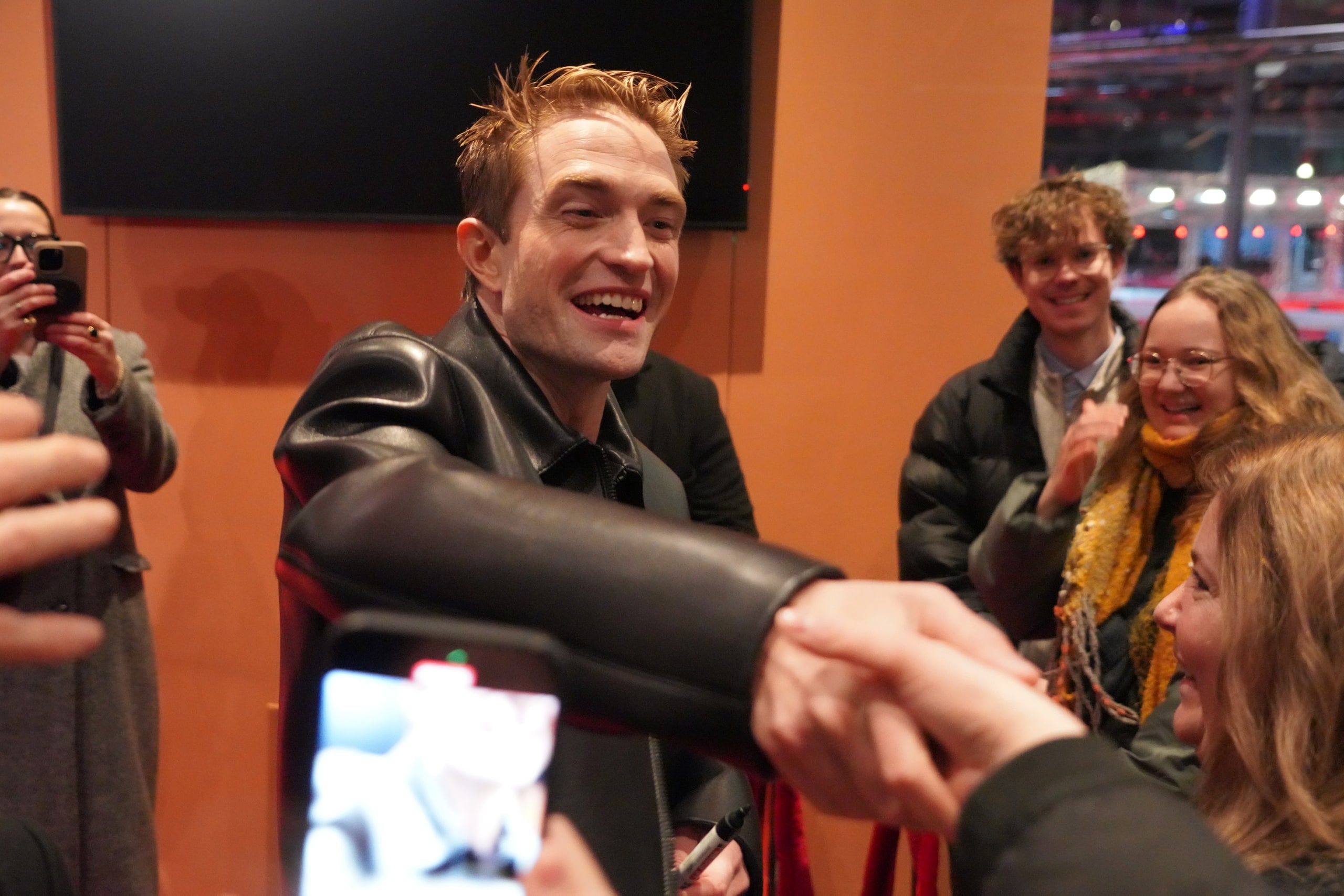 Robert Pattinson laughing as he reaches across the barrier to shake a hand.