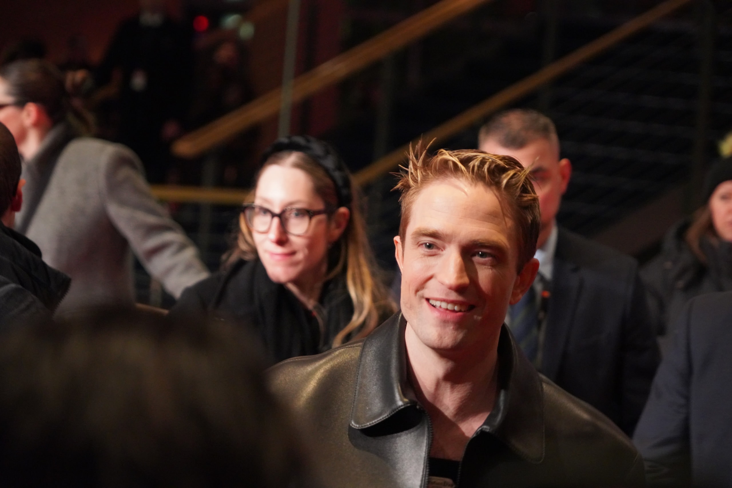 Robert Pattinson smiling in a close portrait amid the crowd at the Mickey 17 premiere.