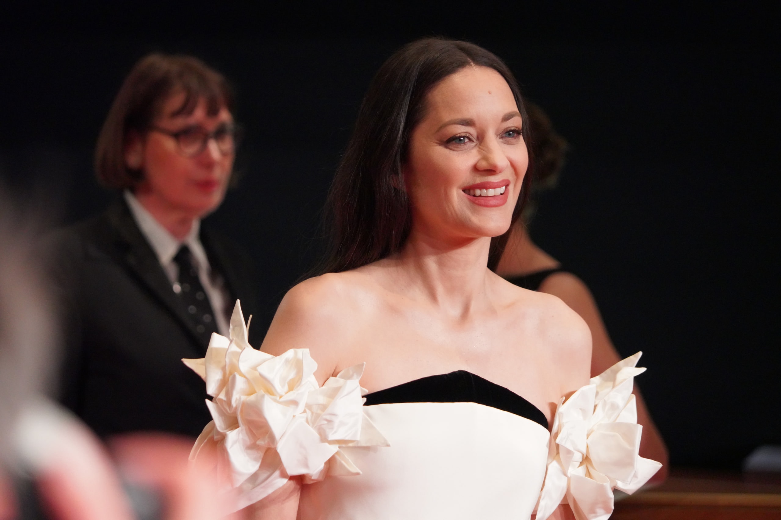 Marion Cotillard smiling in a white sculptural gown on the Berlinale red carpet.