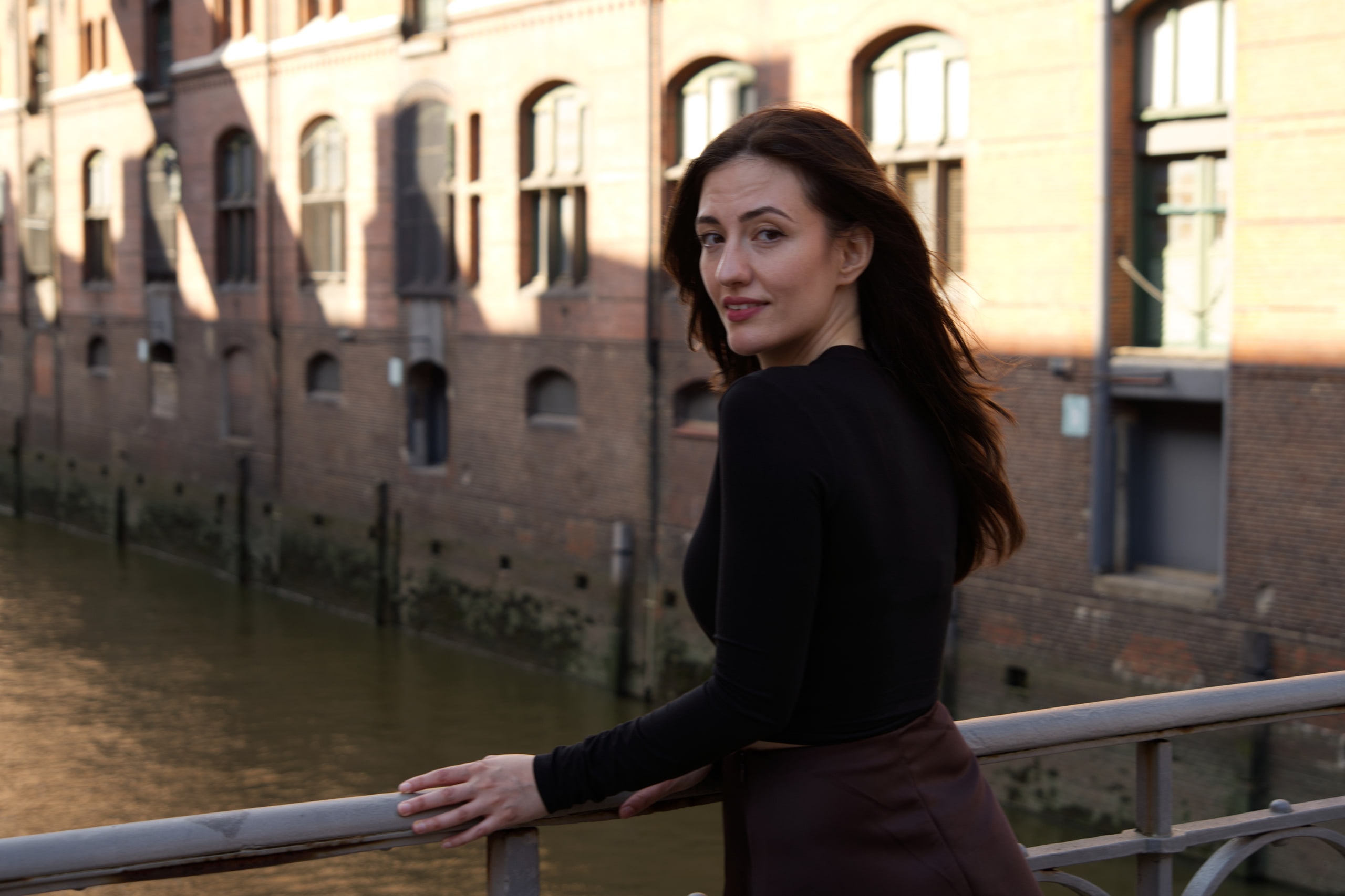 Breshna Hamid Khan looking back toward the camera beside a Hamburg canal, brick buildings behind her.