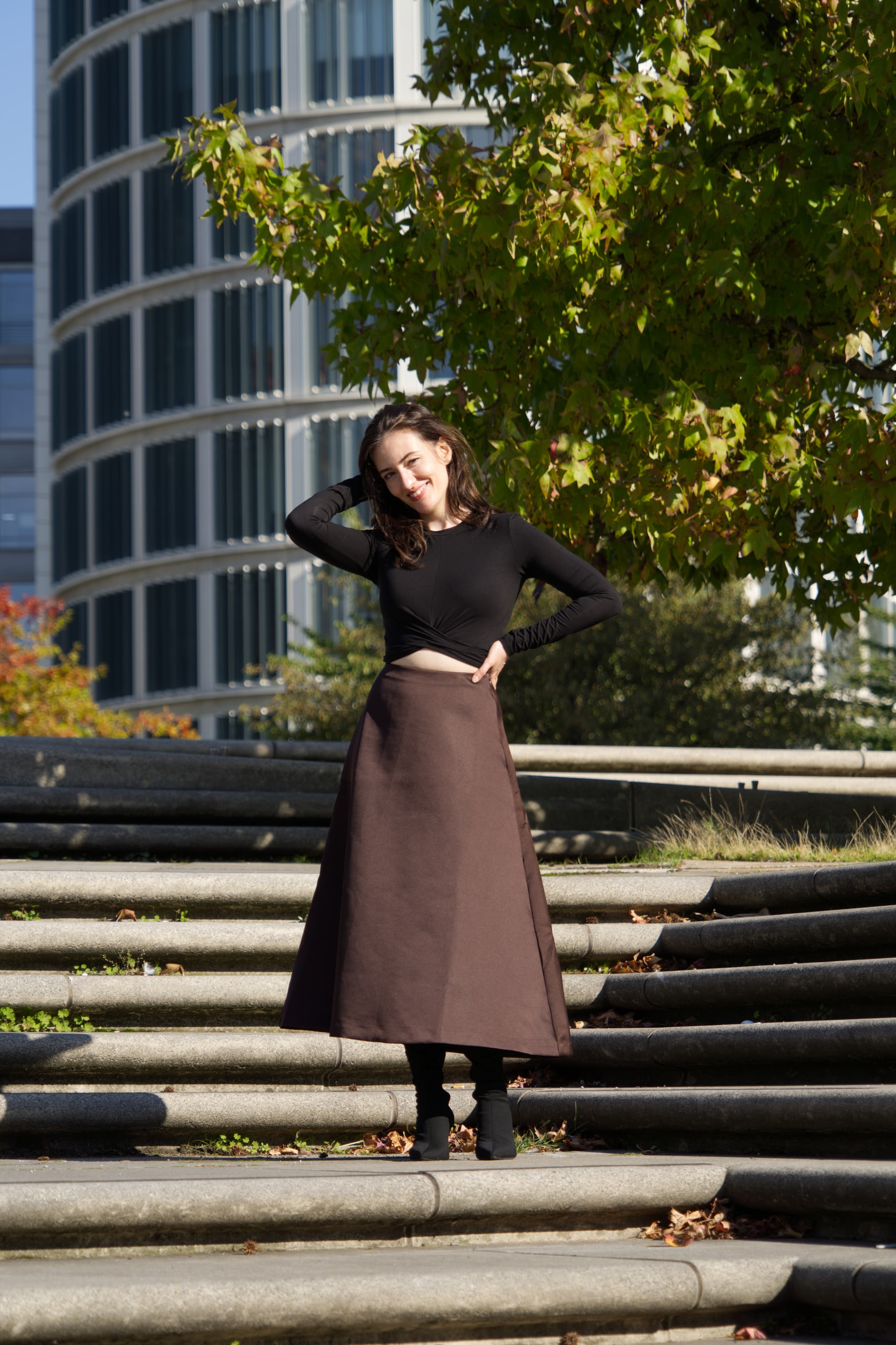 Breshna Hamid Khan standing on wide steps beside trees and glass buildings.