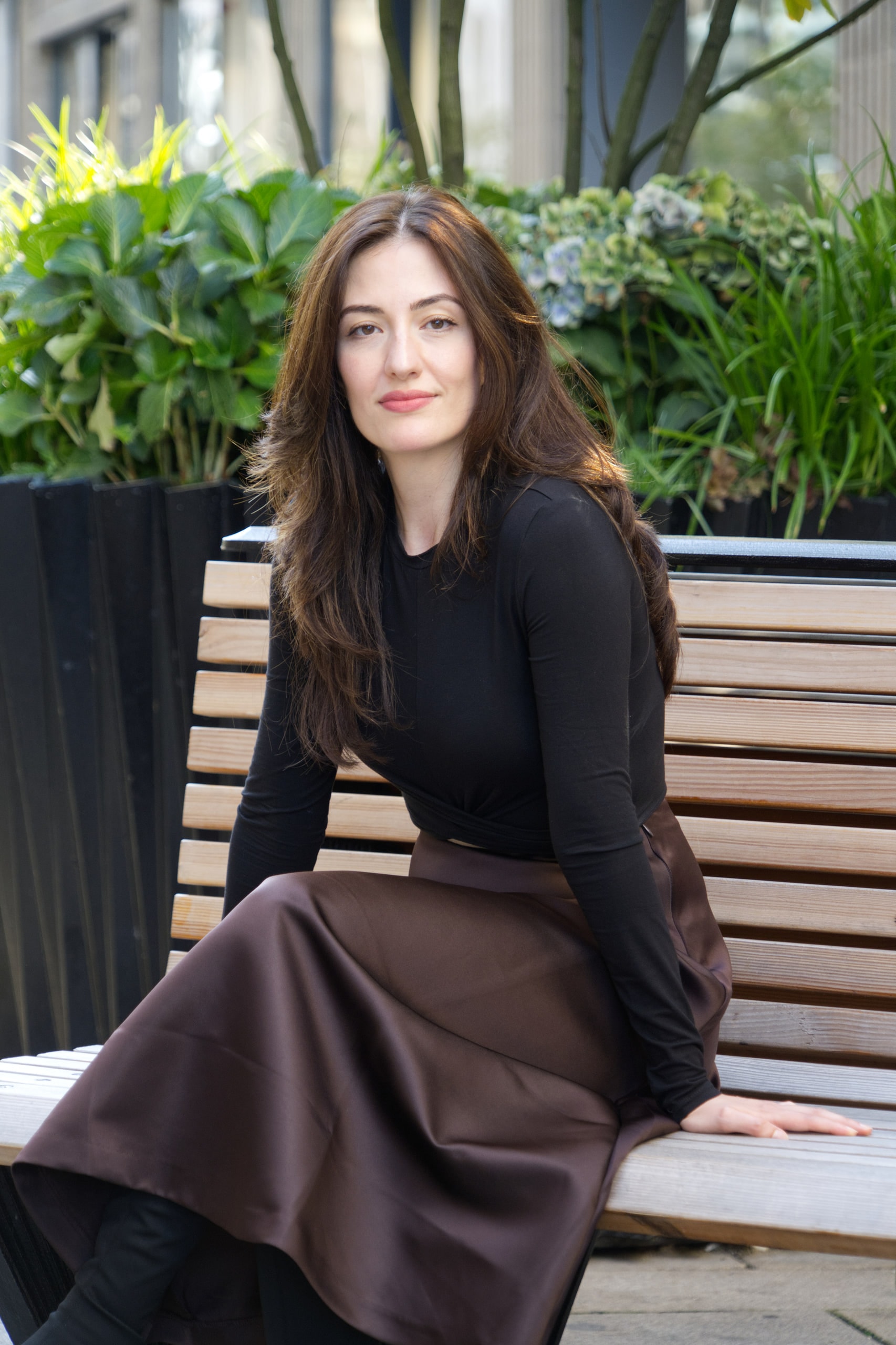 Breshna Hamid Khan seated on a wooden bench, her brown skirt spread across the seat.