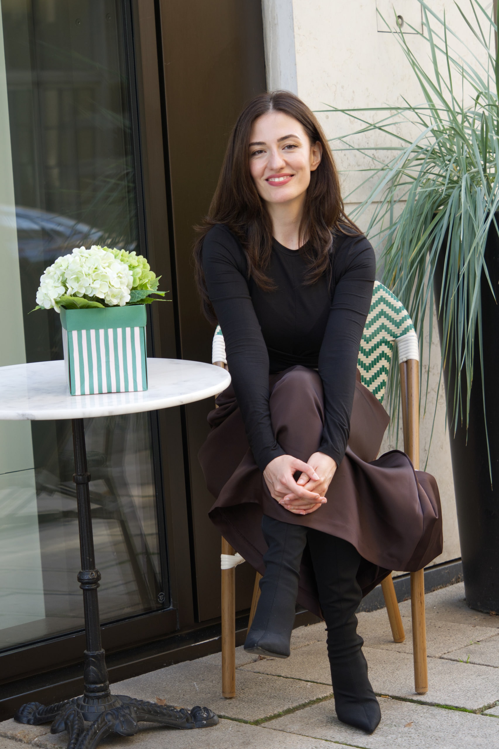 Breshna Hamid Khan smiling outside a cafe beside a small table and white flowers.