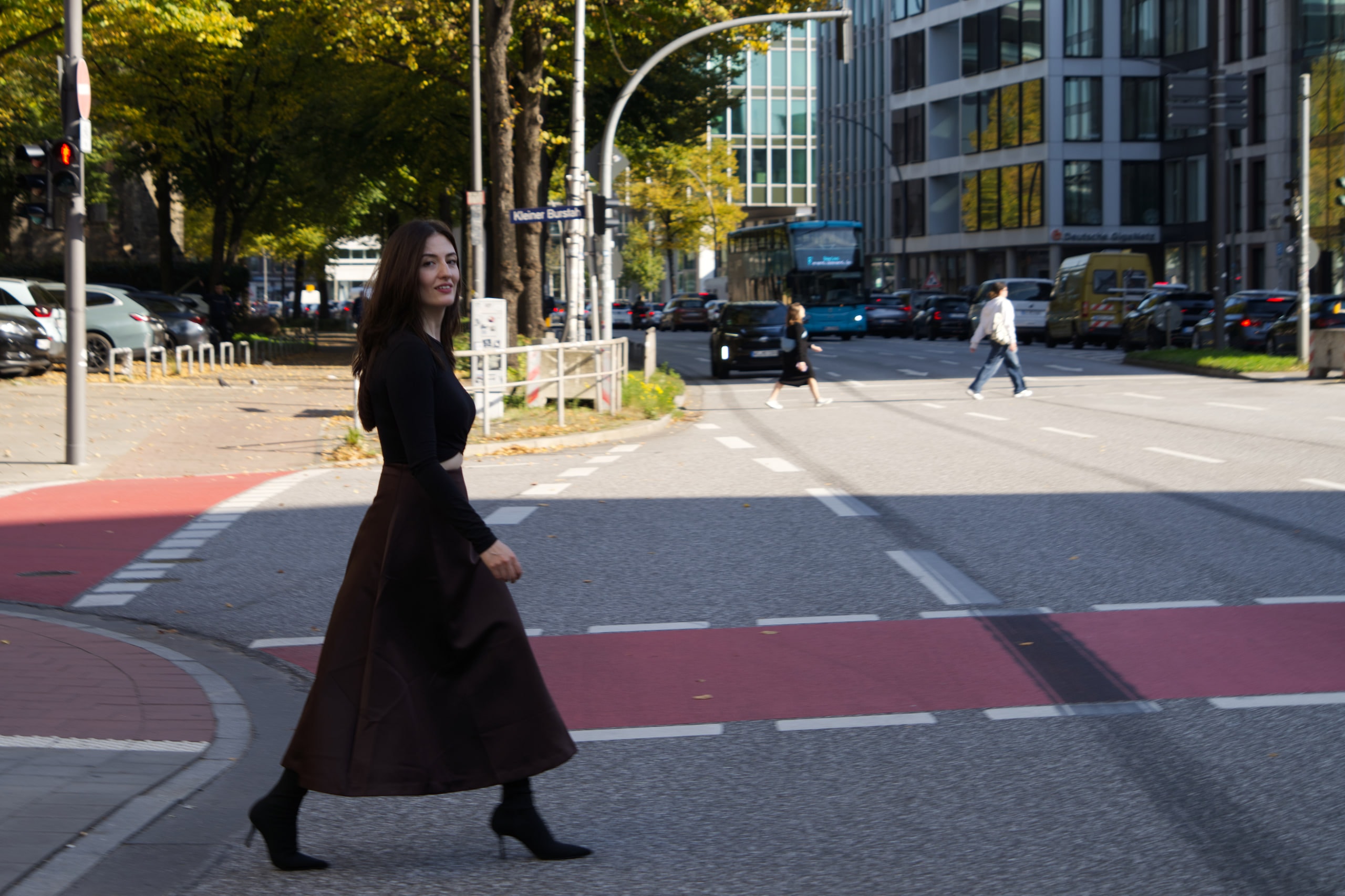 Breshna Hamid Khan walking across a Hamburg street, her brown skirt moving with her stride.