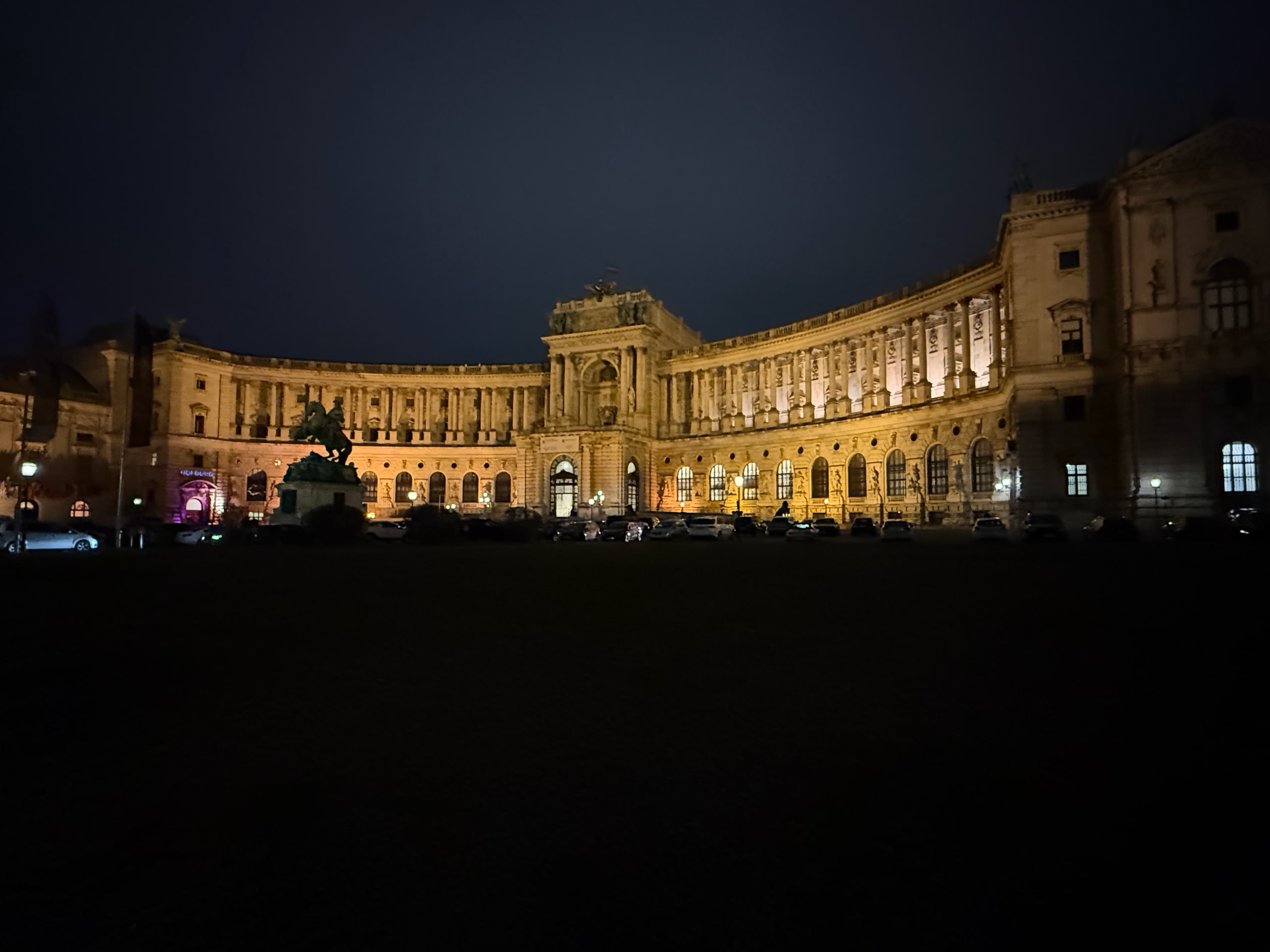 The curved facade of the Neue Burg illuminated across Heldenplatz at night.
