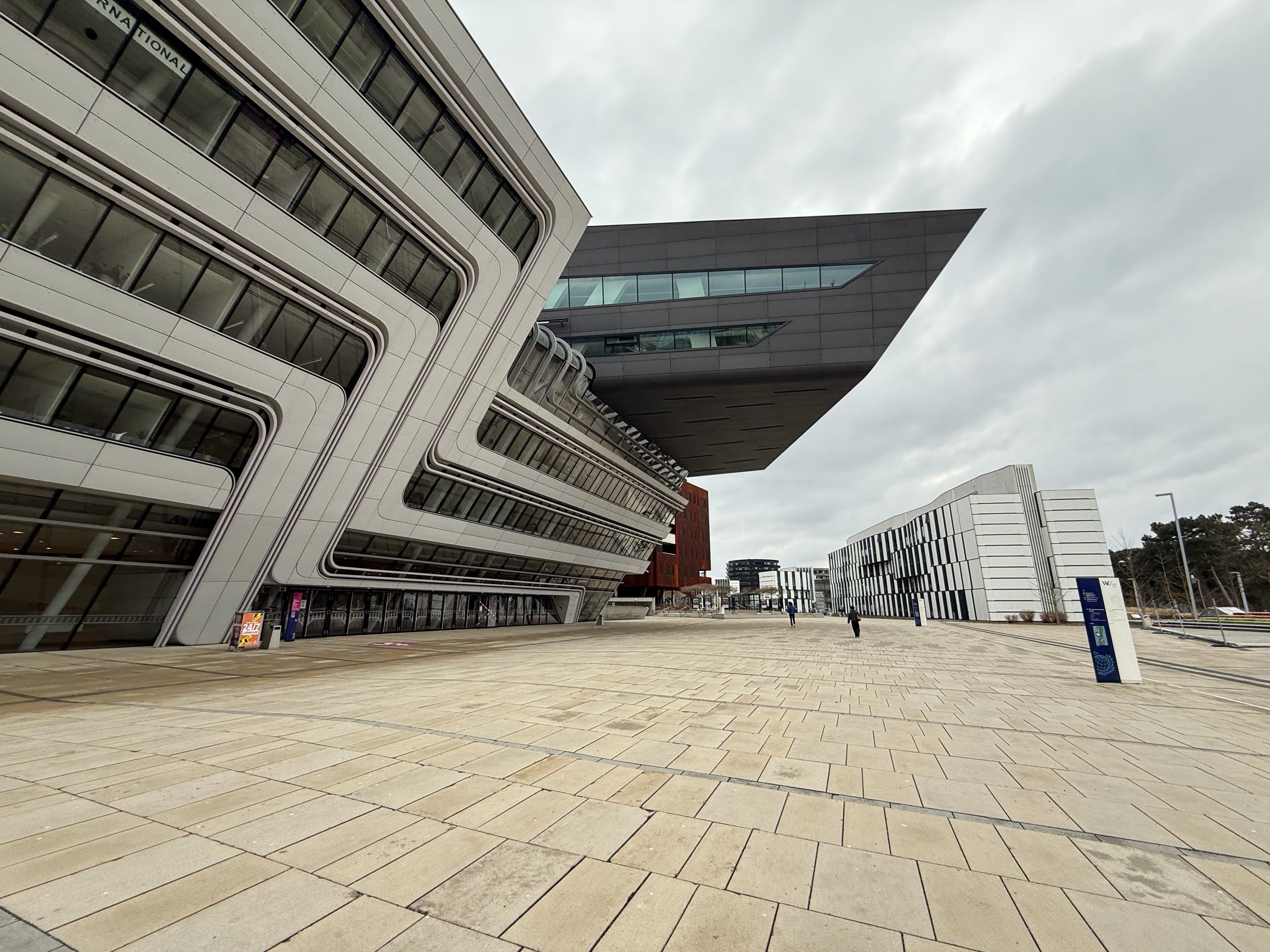 Angular white university buildings framing an open plaza beneath a grey sky.