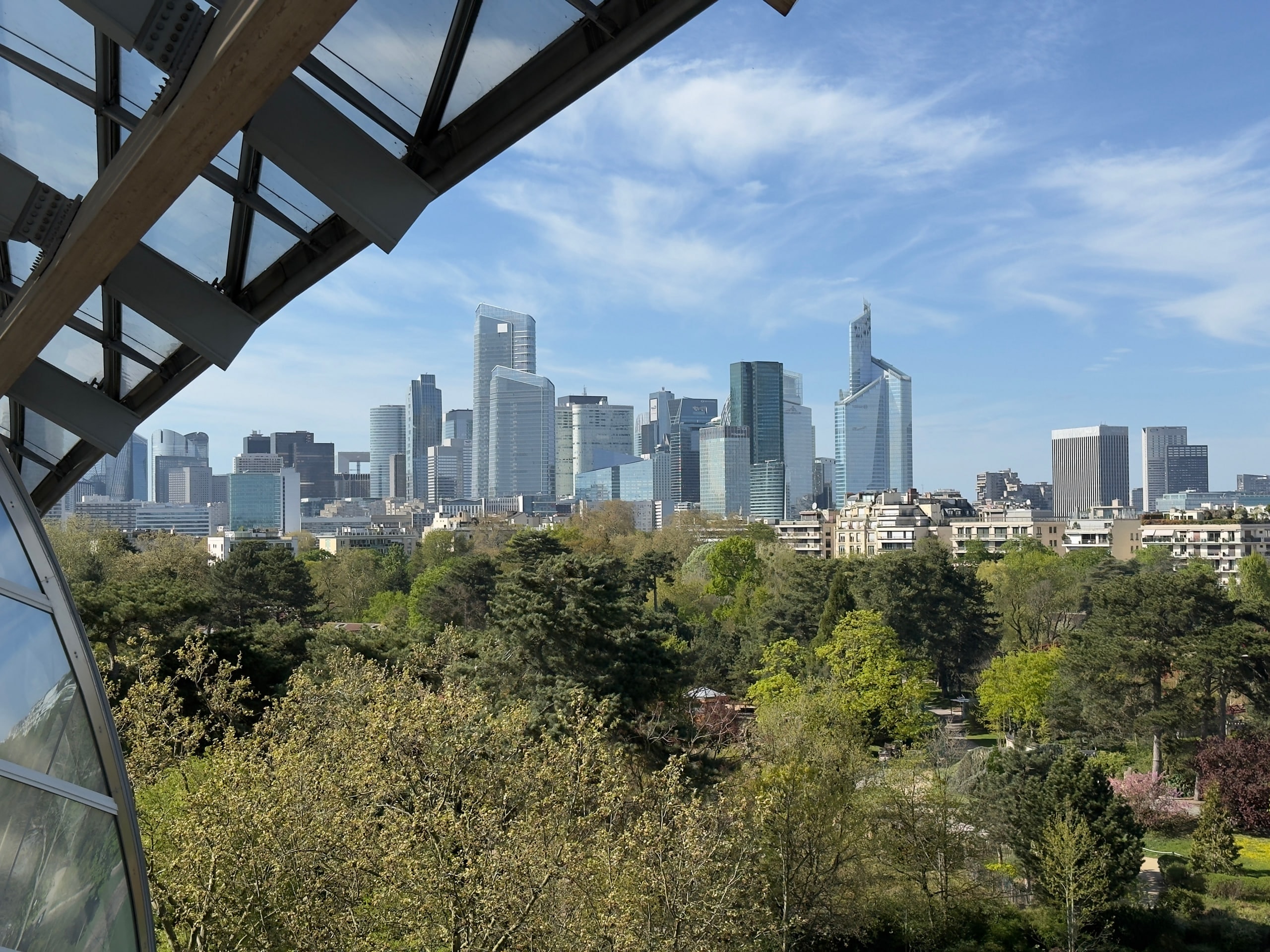 The La Défense skyline beyond trees and angular structural beams.