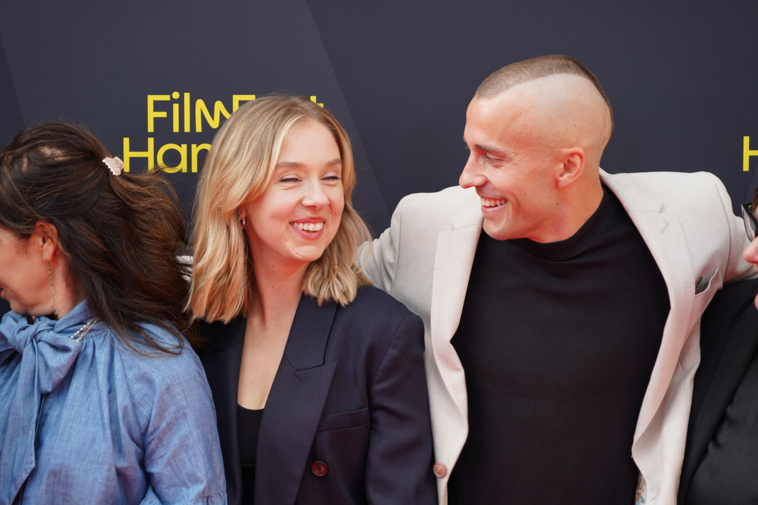 Two members of the Nine to Five — Das Amt team turning toward each other and laughing on the red carpet.