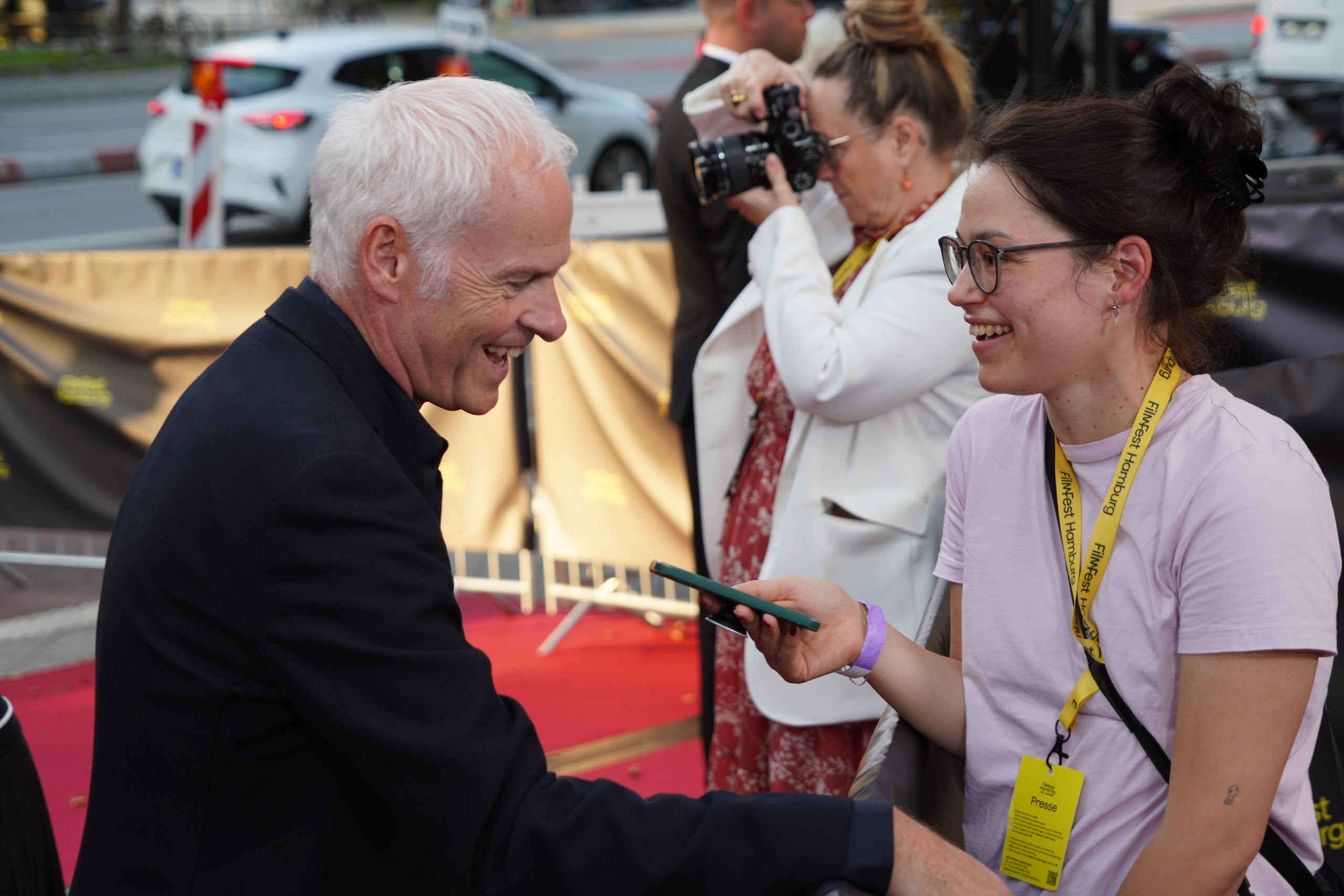 Martin McDonagh laughing while speaking with an interviewer holding a recorder beside the red carpet.