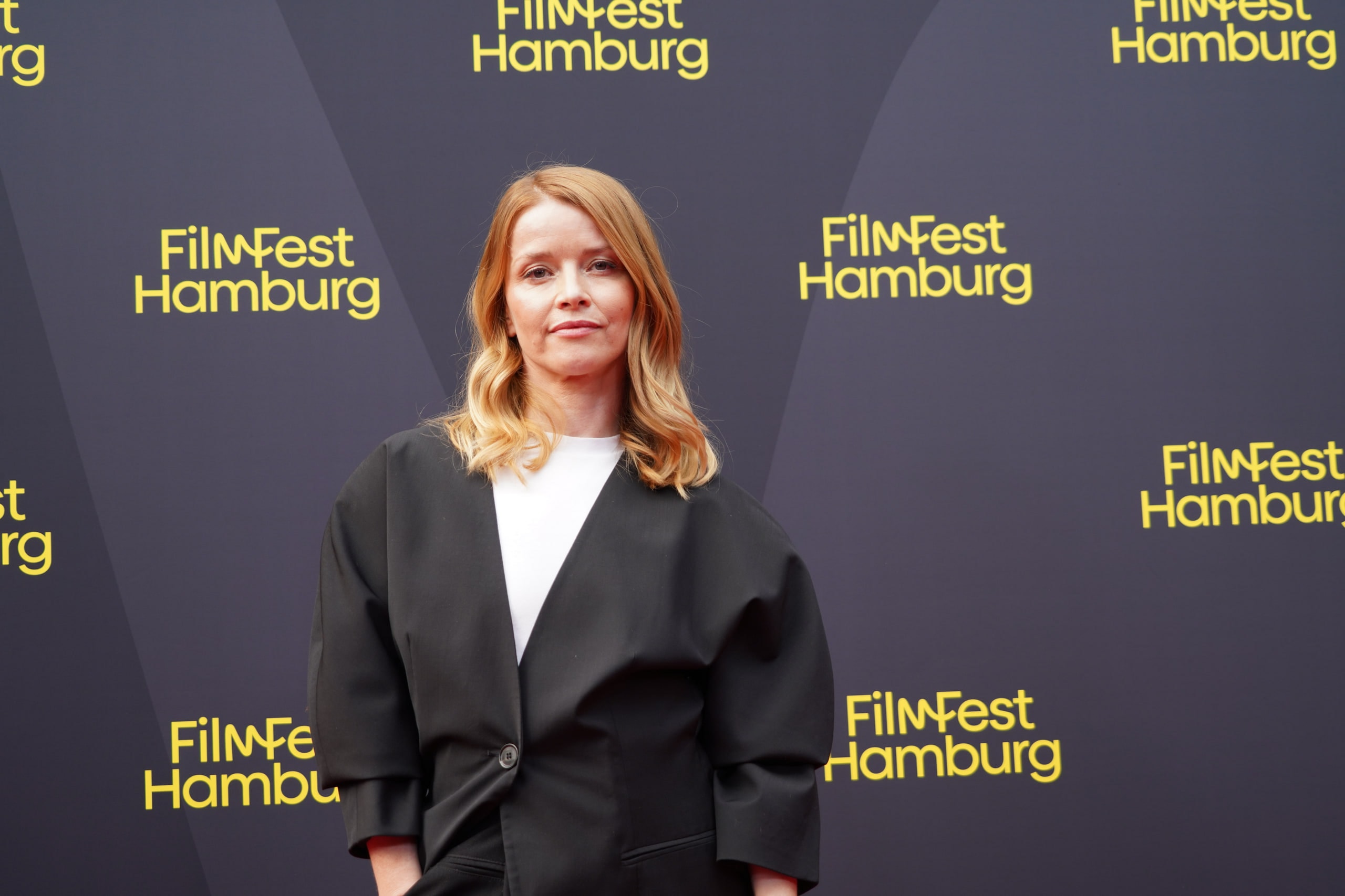 Karoline Schuch in a black jacket and white top, looking toward the camera on the red carpet.