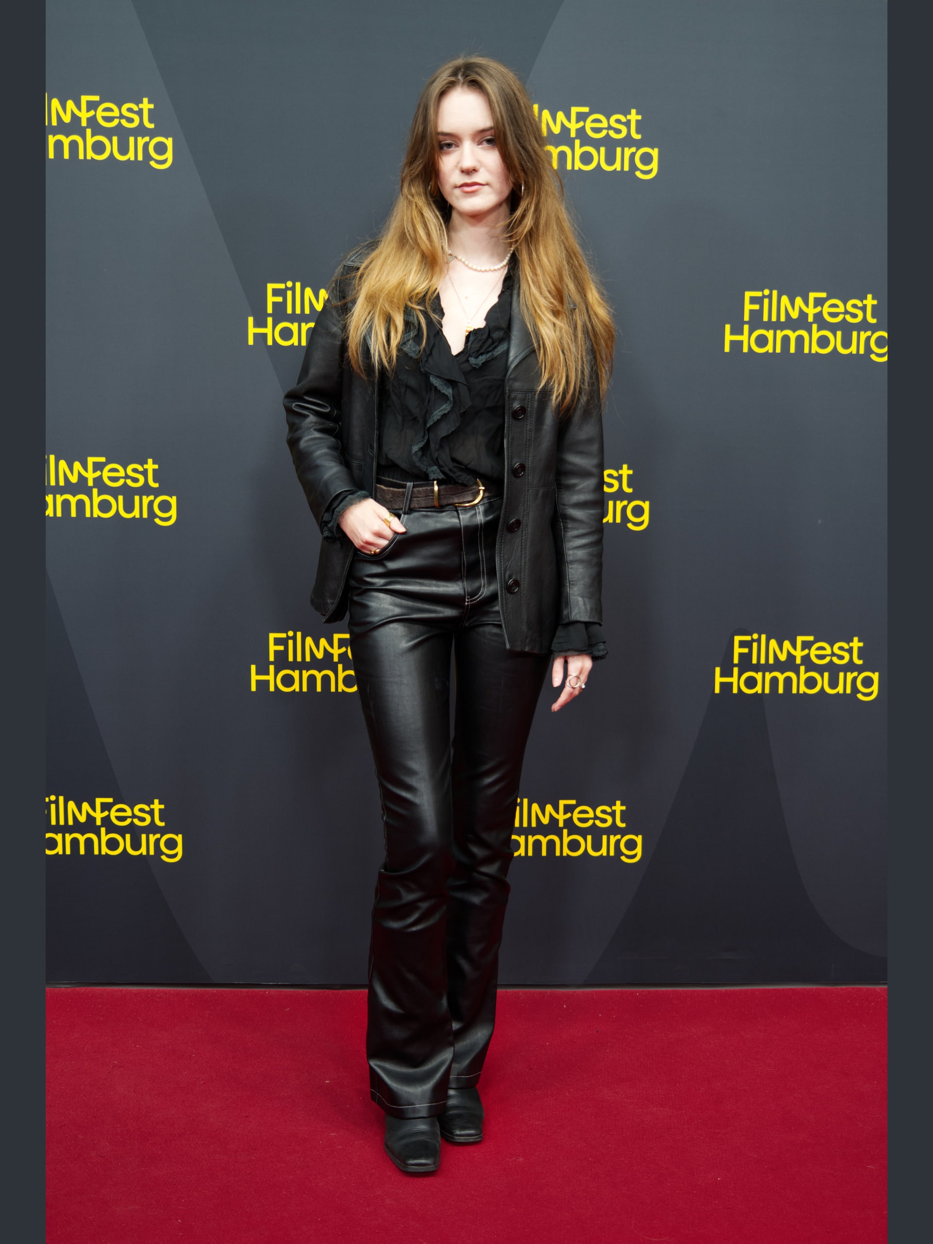 Full-length portrait of Rebecca Schulz in a black leather jacket and trousers on the red carpet.