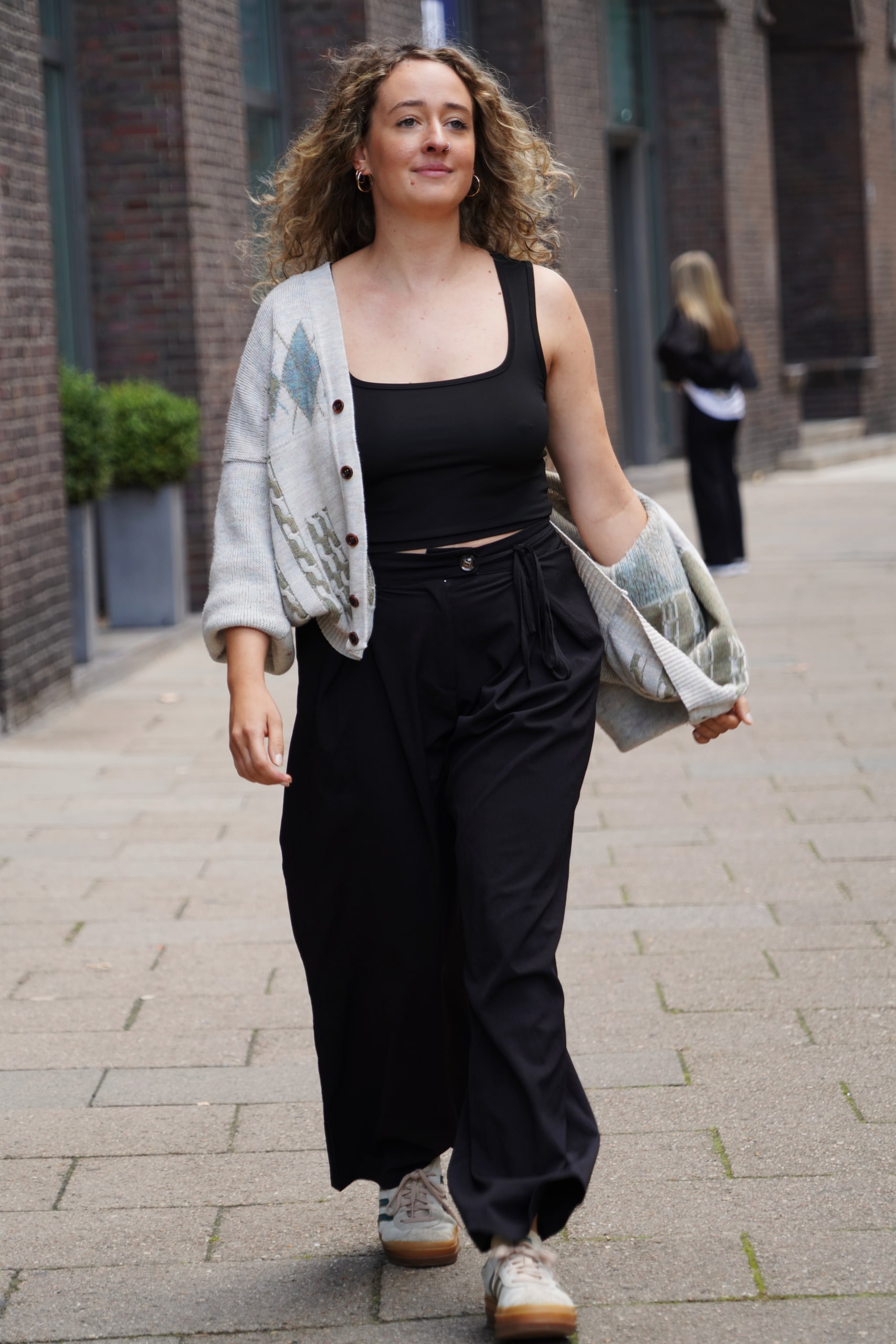 Larissa Kählert walking toward the camera beside Hamburg's brick arcades, her grey cardigan falling from one shoulder.