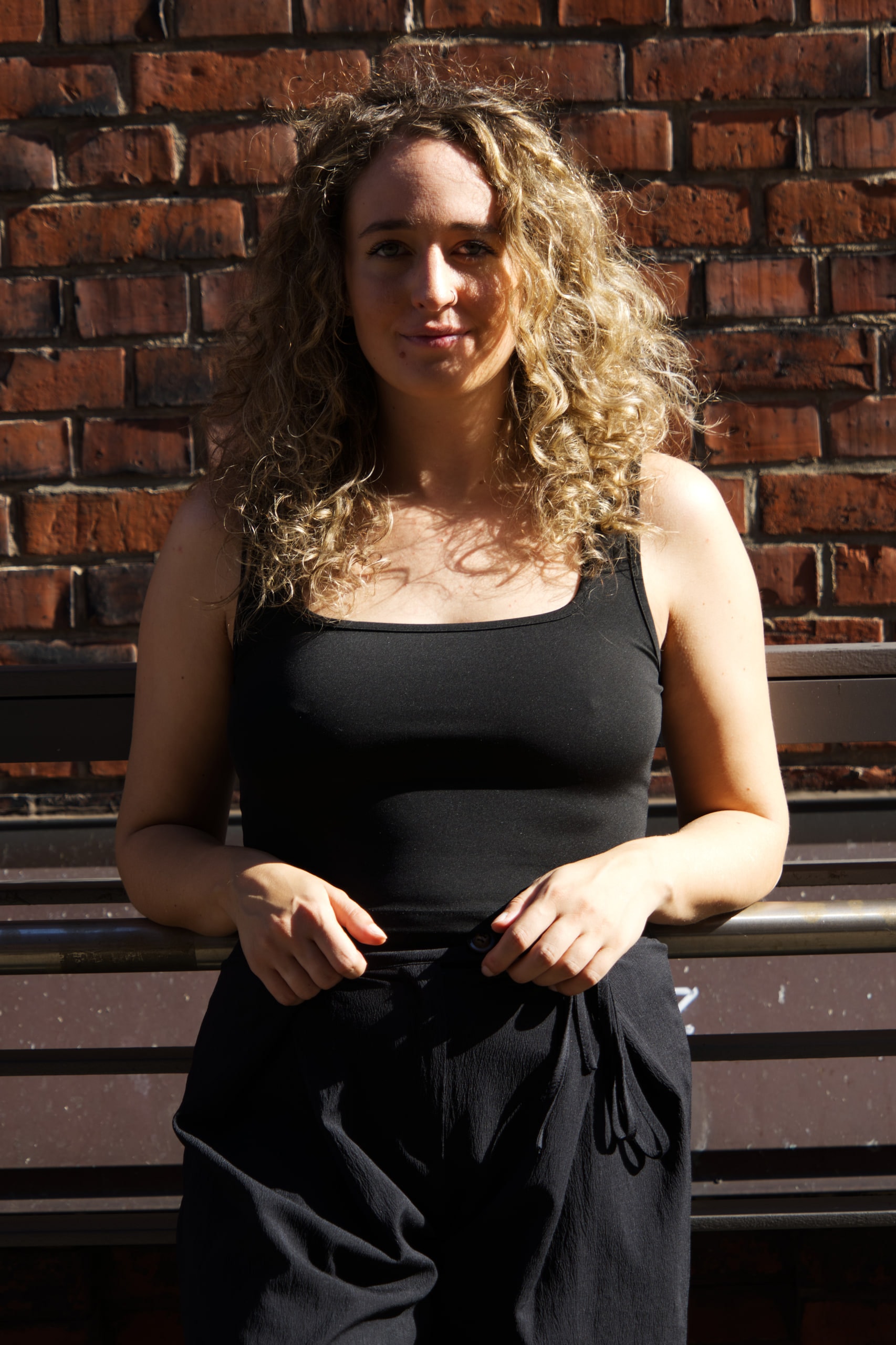 Larissa Kählert facing the camera in a black top against sunlit brick, with shadow across her face.