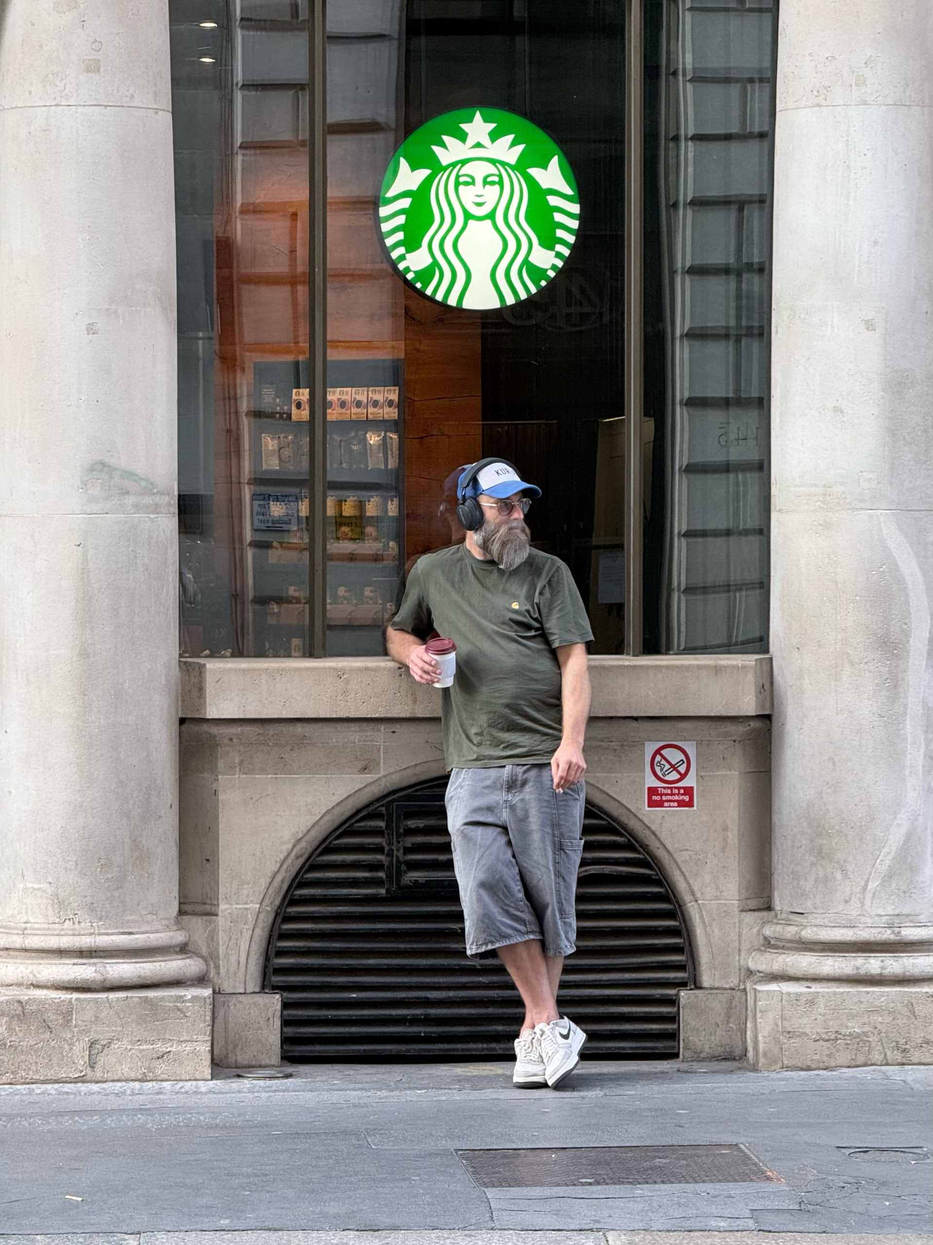 A man leaning against a stone column outside a café in the early morning.
