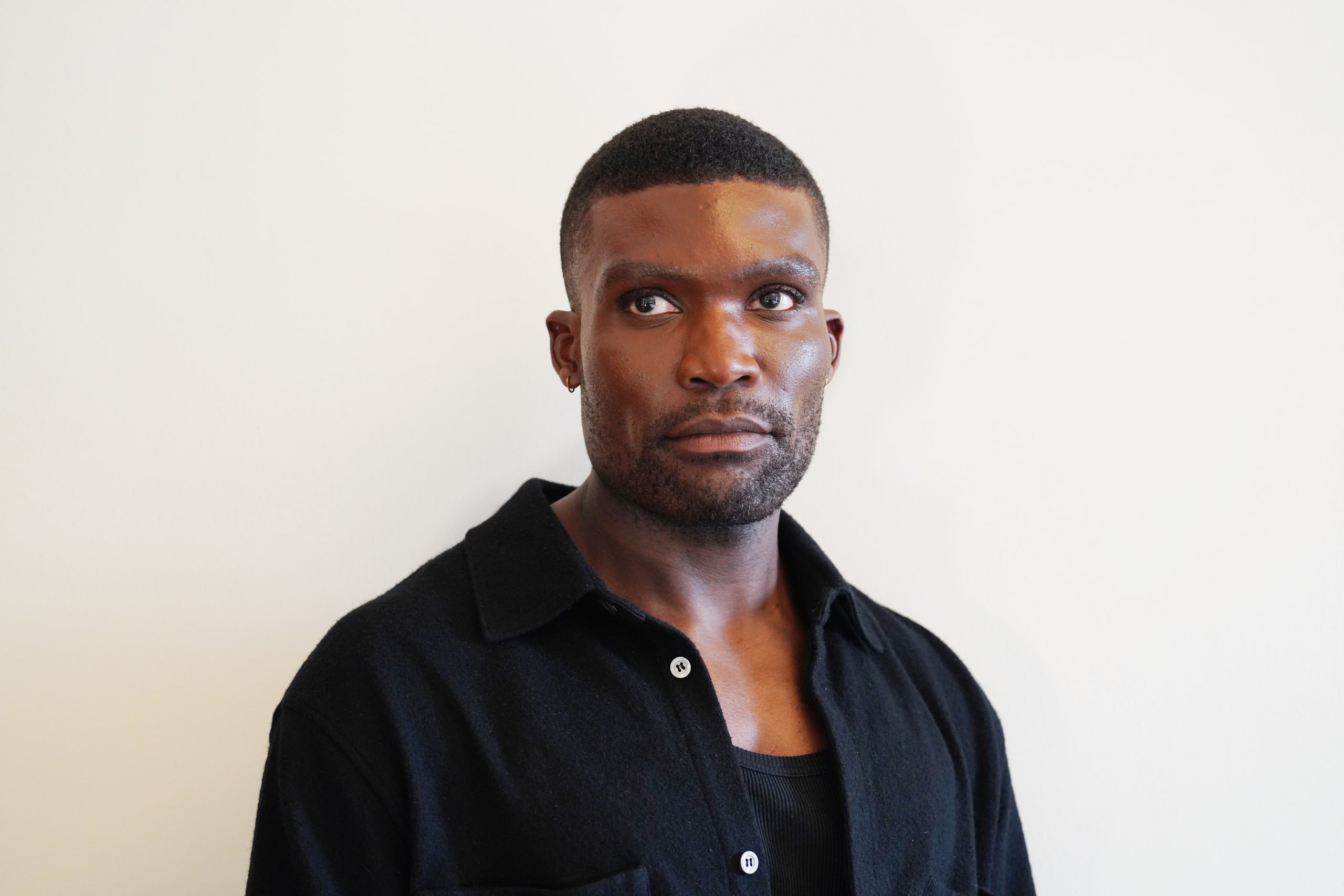 Michael Solomon looking to one side in a black shirt against a pale wall.