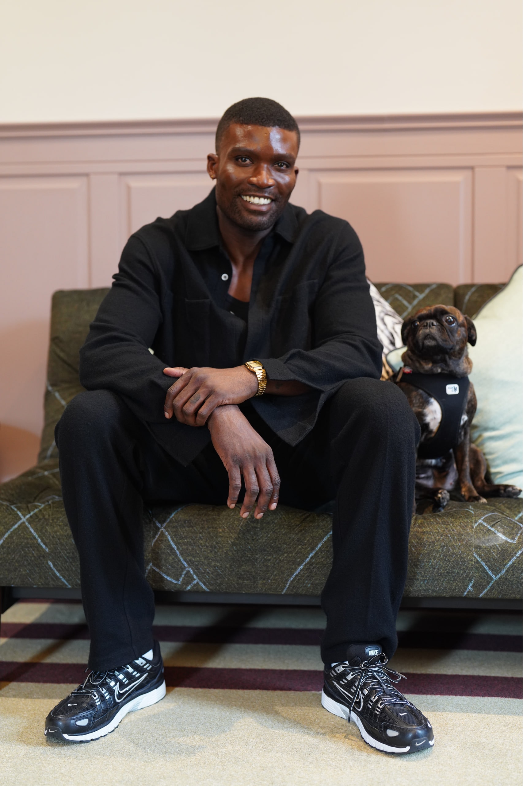 Michael Solomon smiling on a patterned sofa with a small dog beside him.