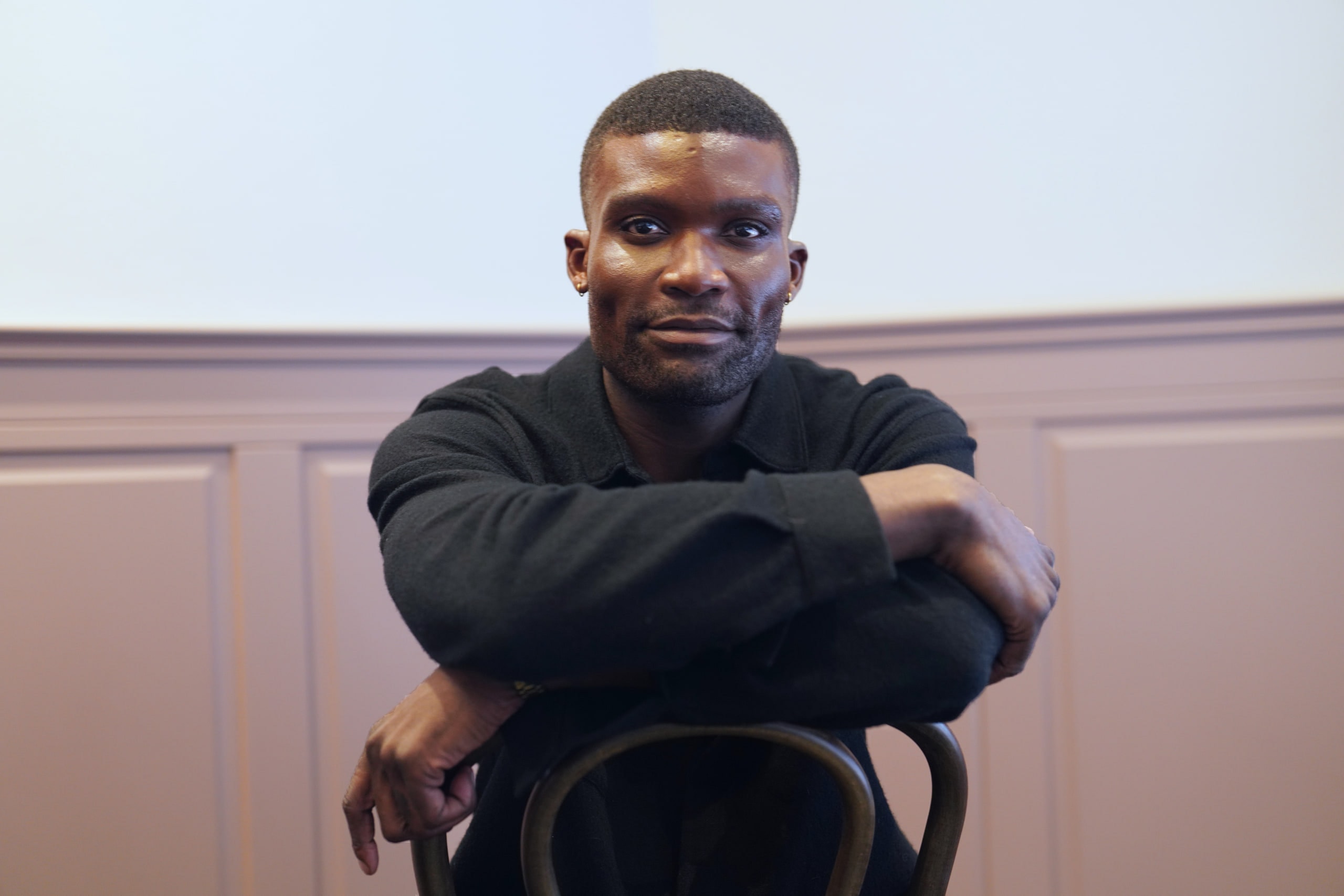 Michael Solomon resting his arms across the back of a chair beneath pink wall panelling.