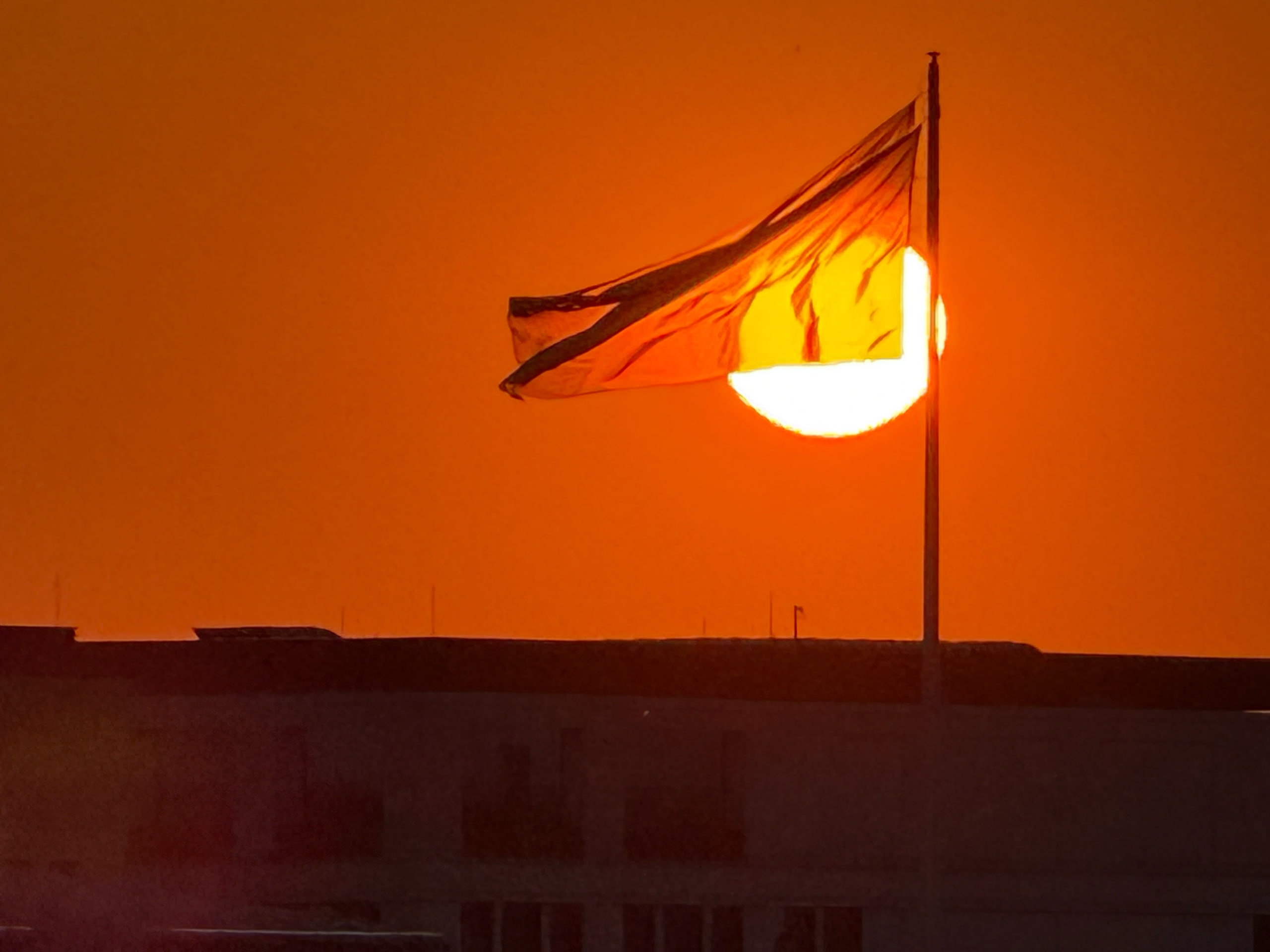 A flag catching the last of the sun, both reduced to silhouette.