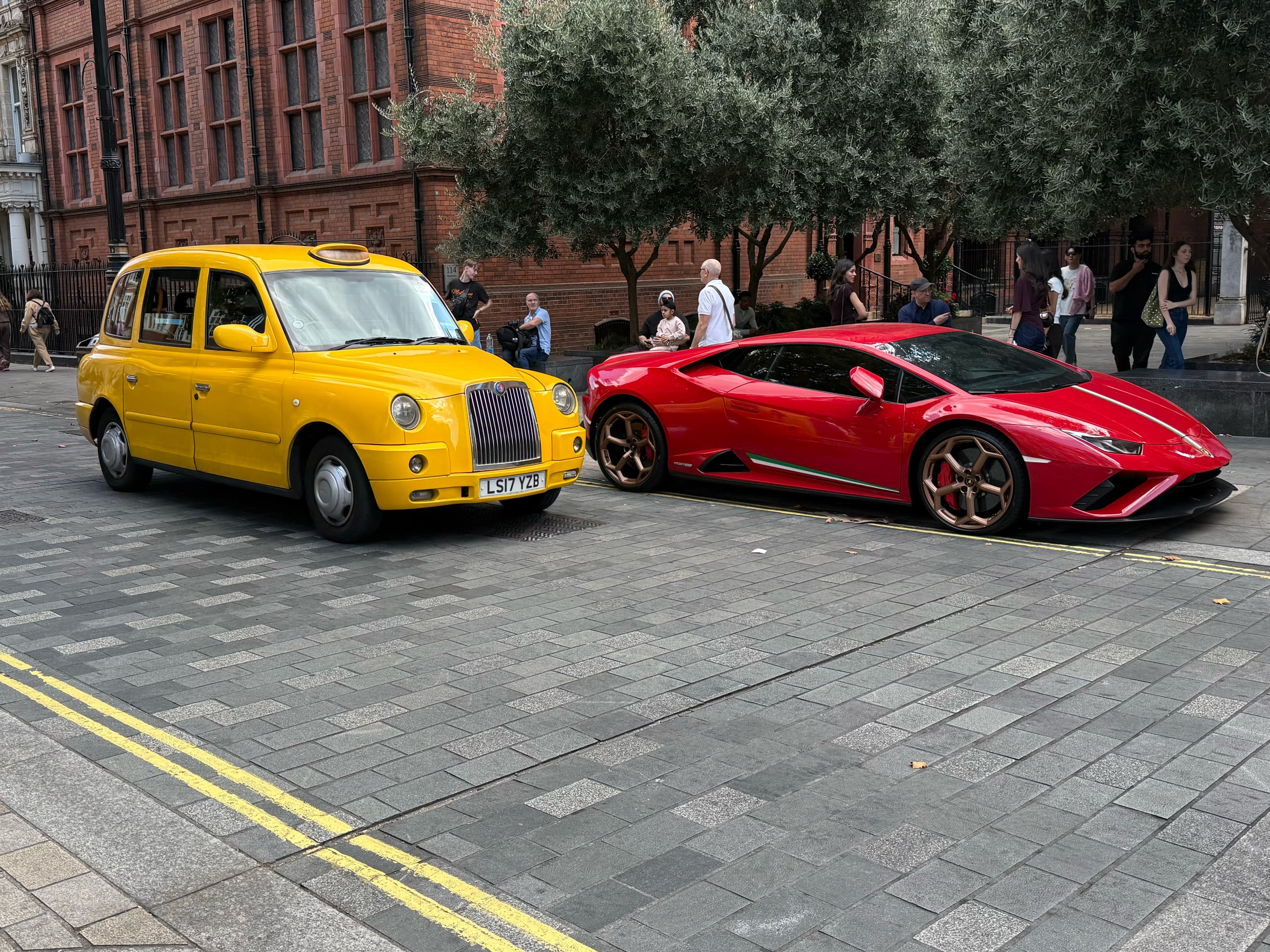 A yellow taxi and a red sports car waiting at a kerb.