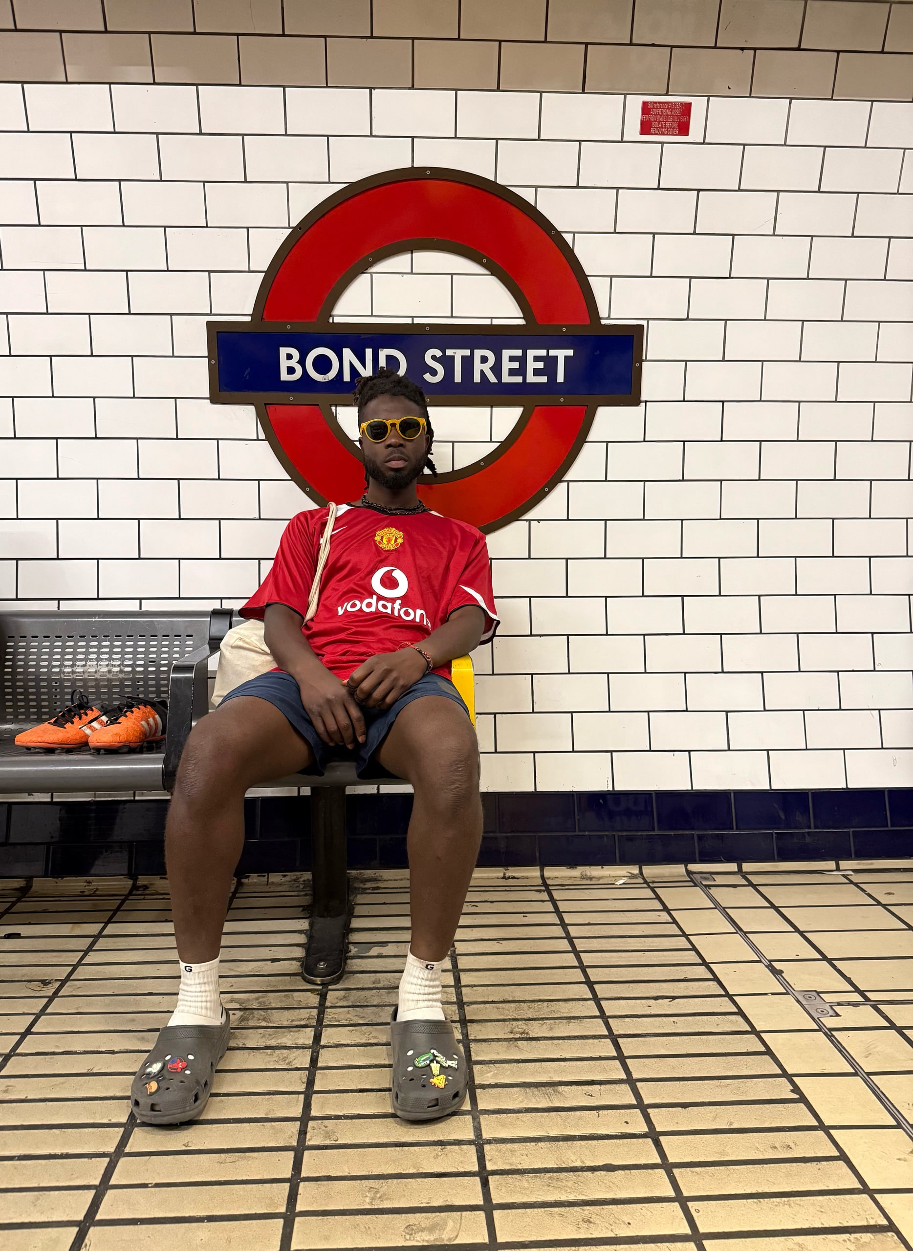A man in a football shirt sitting beneath the Bond Street roundel.