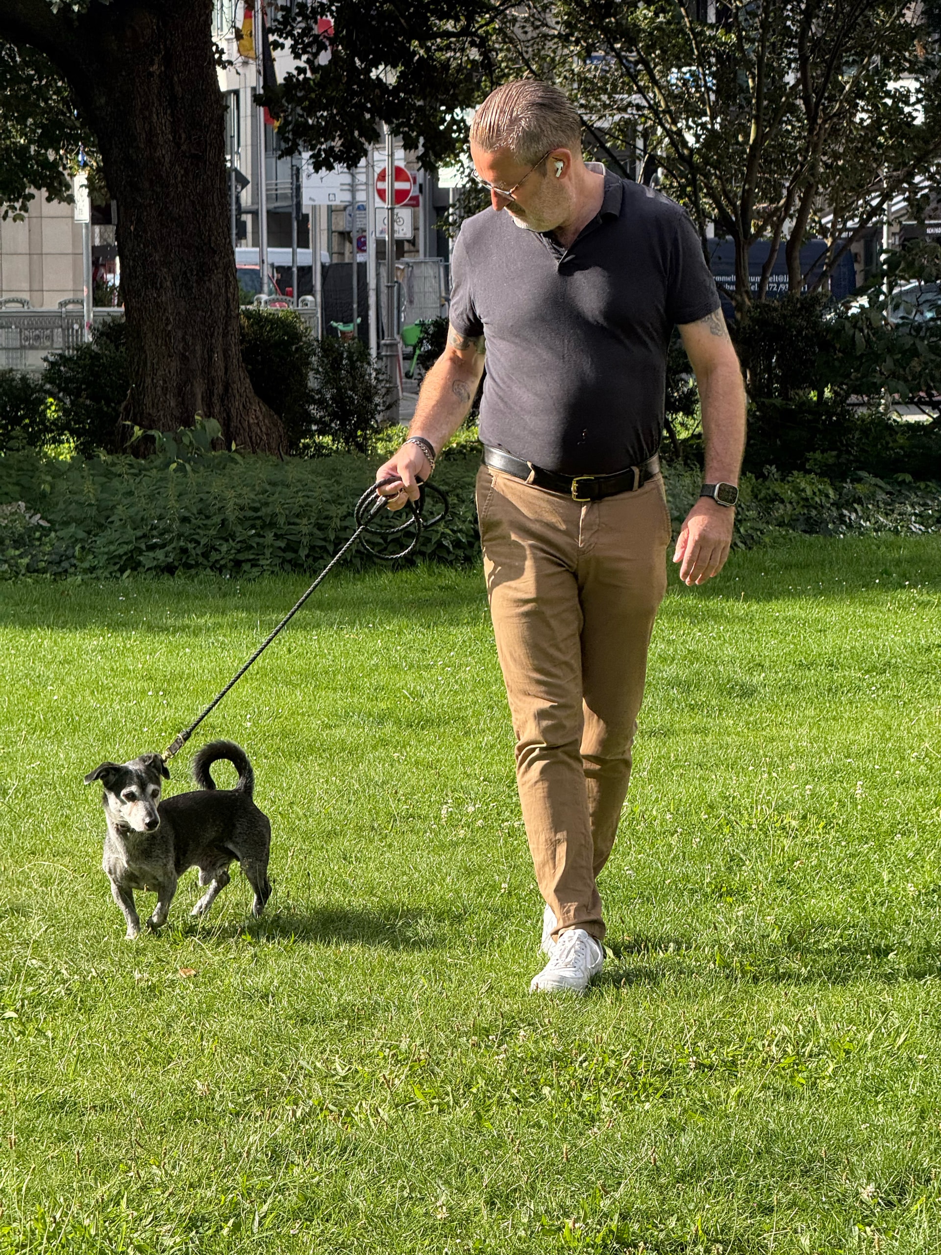 A man walking a dog across open grass in the morning.