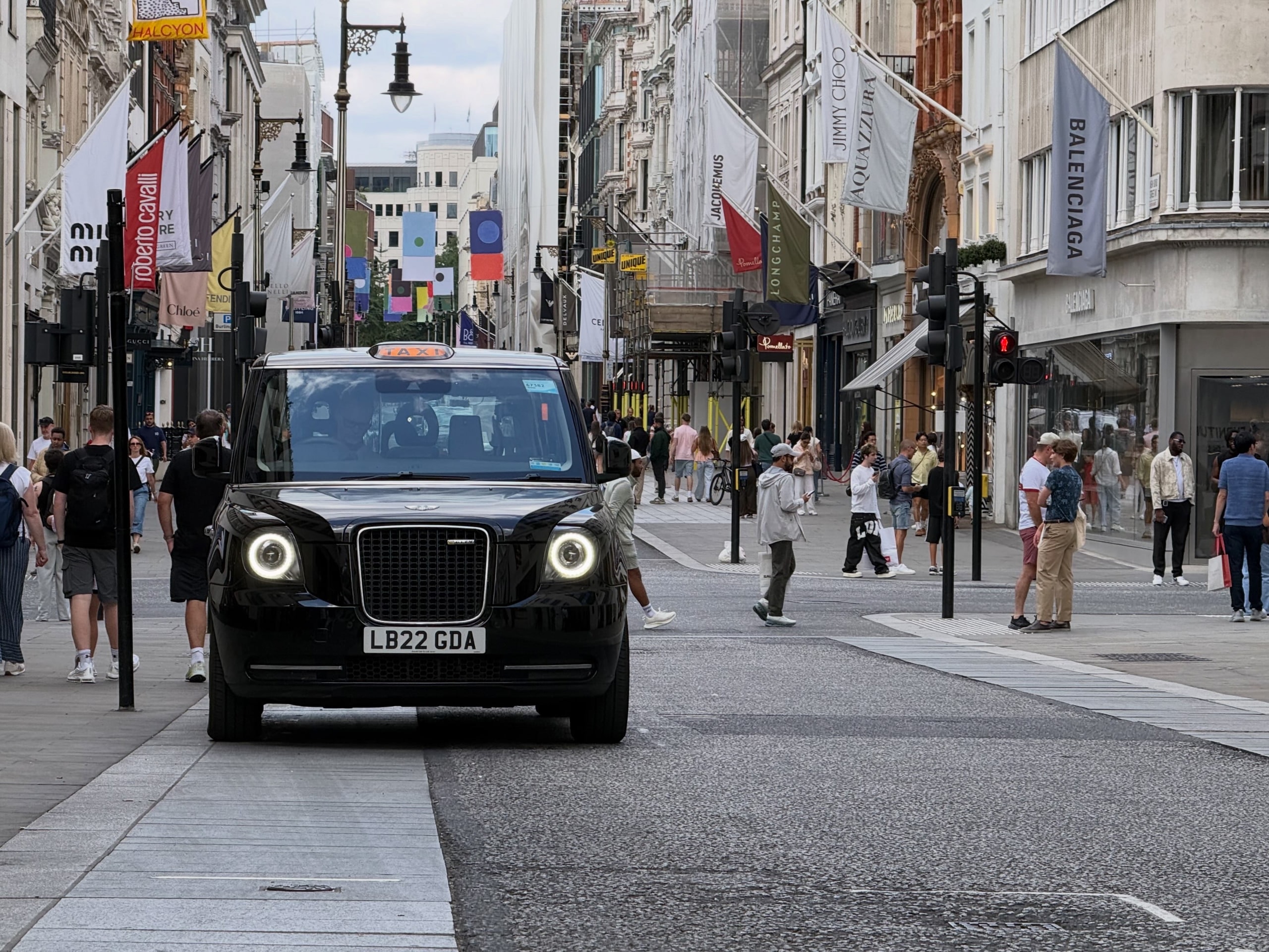 A black cab waiting on a shopping street lined with storefronts.