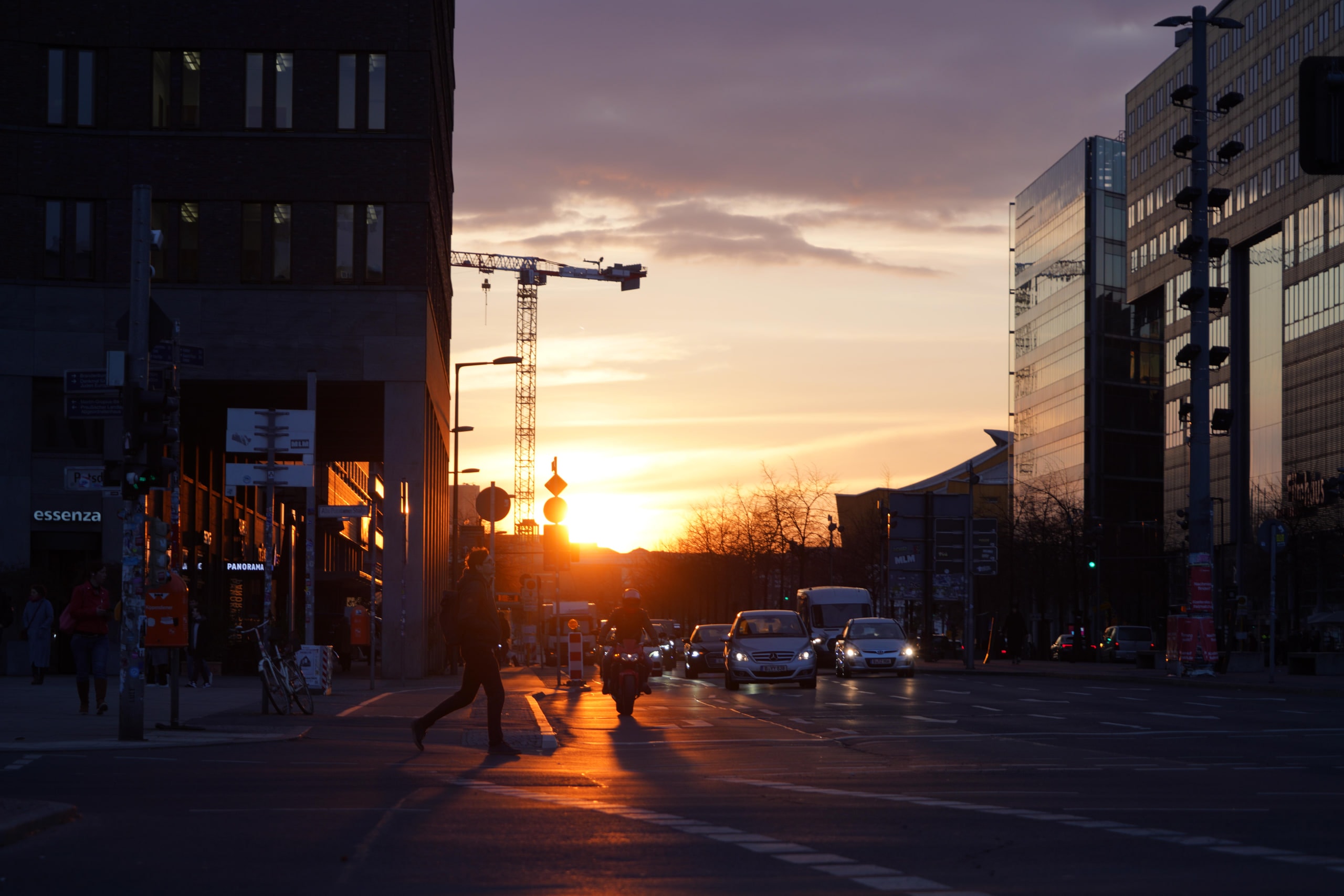 A figure crossing an empty junction as the sun drops behind a crane.