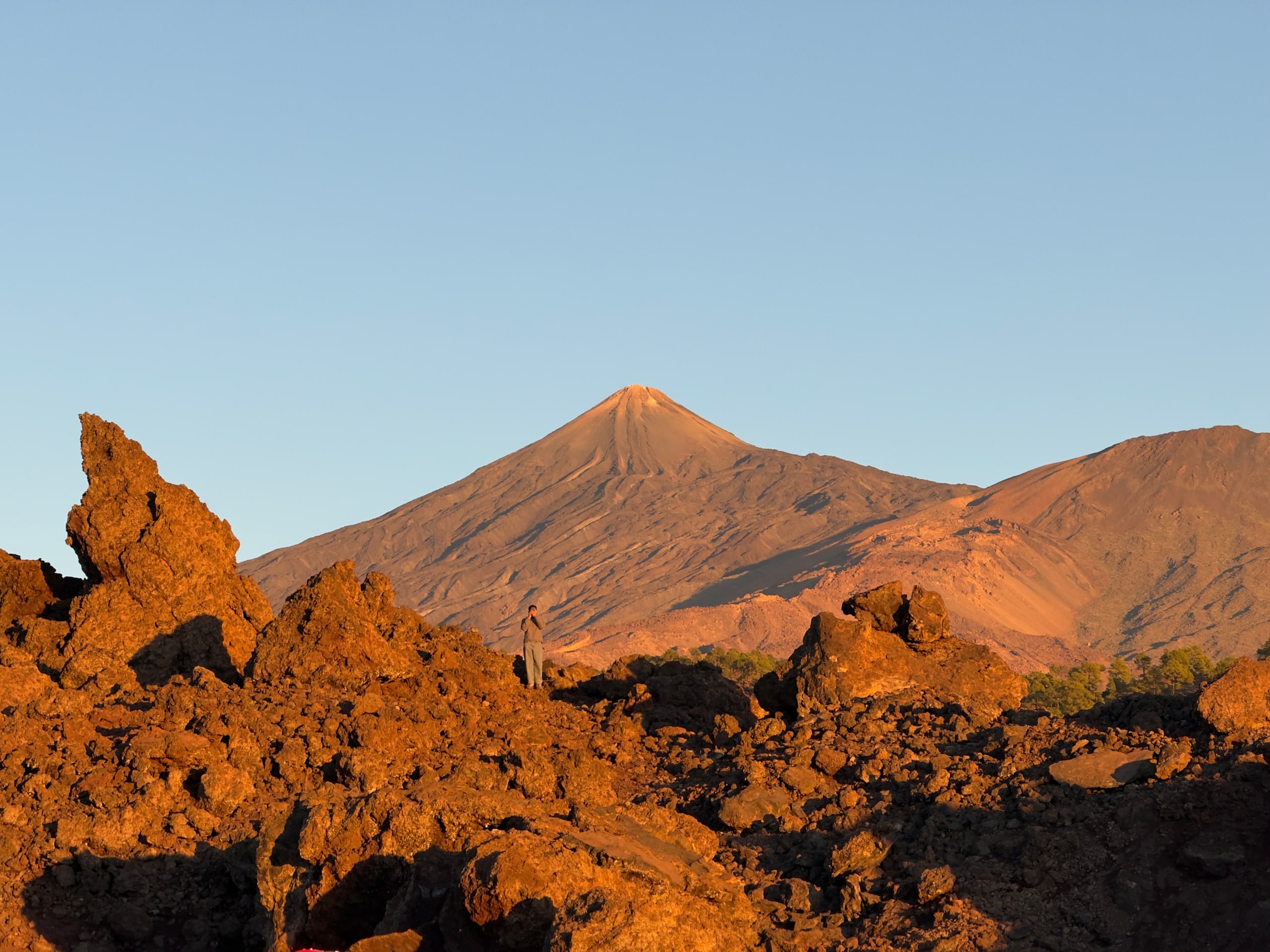 Mount Teide catching warm evening light above dark volcanic rocks.