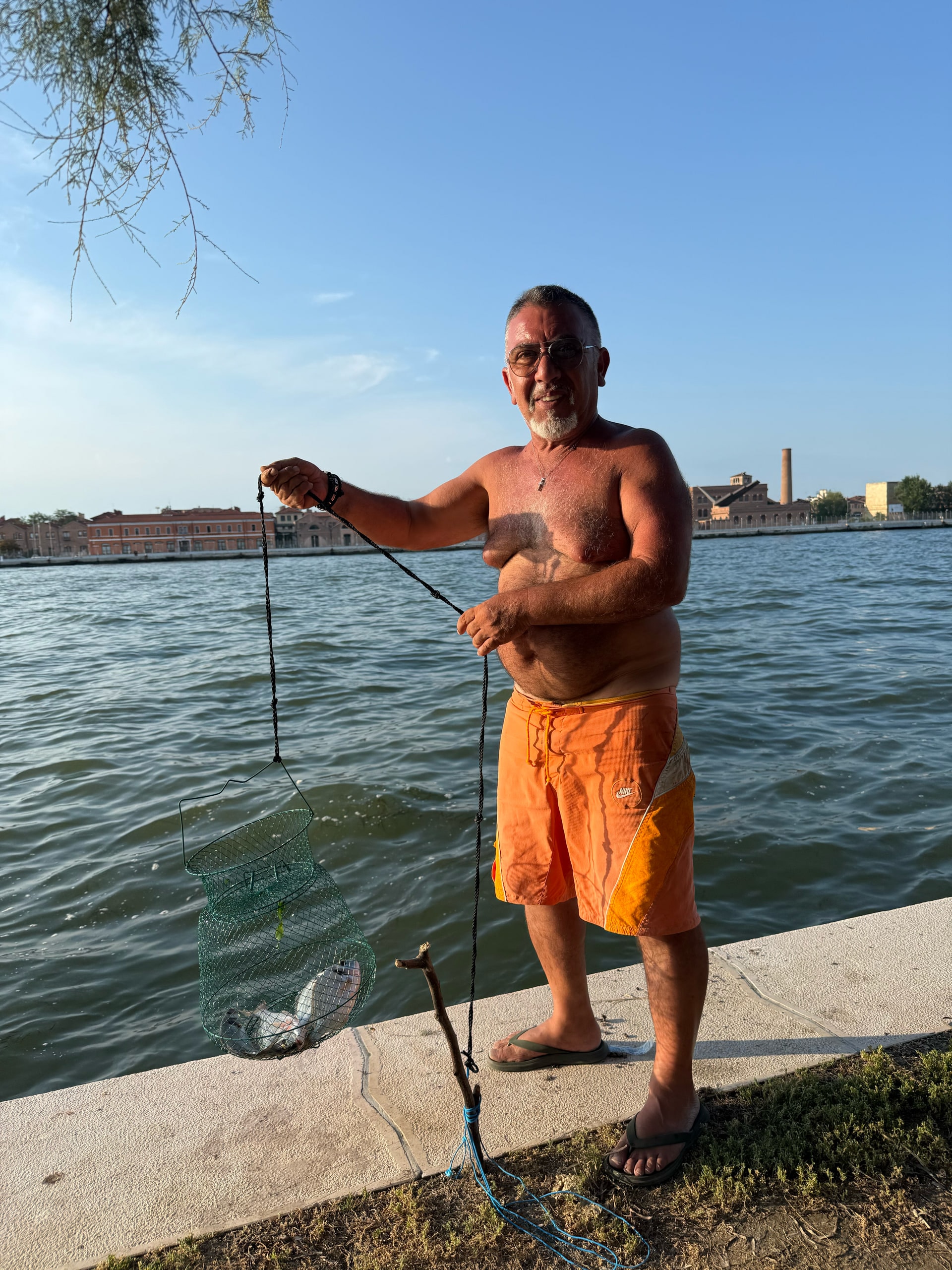 A fisherman standing at the water's edge holding a keepnet.