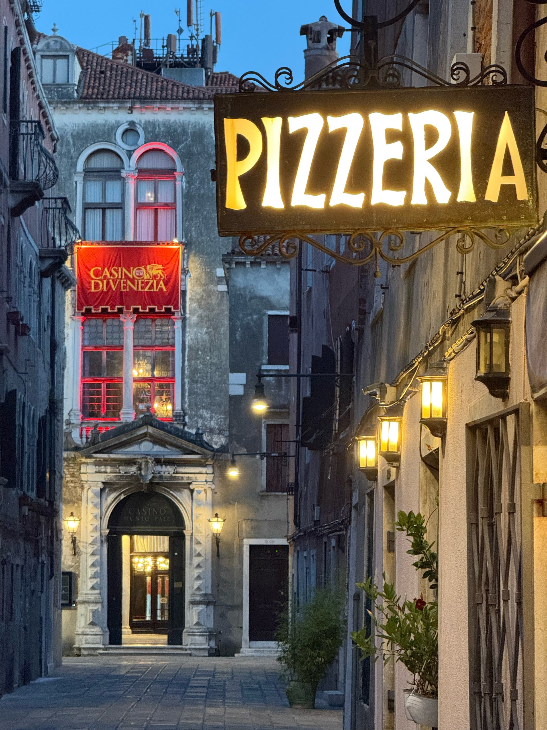 A neon pizzeria sign glowing in a narrow street at dusk.