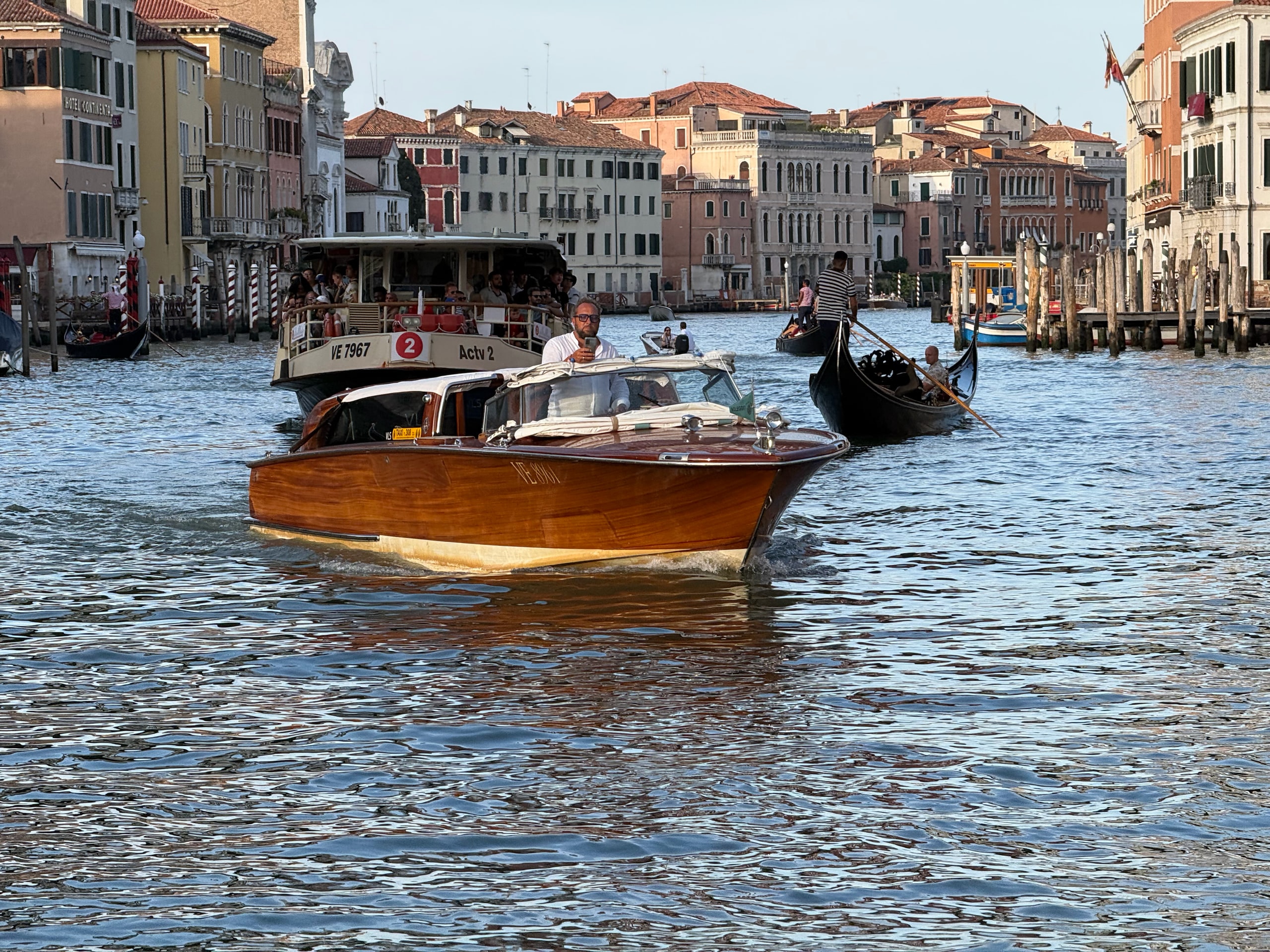 A polished wooden water taxi crossing the Grand Canal among vaporetti and gondolas.