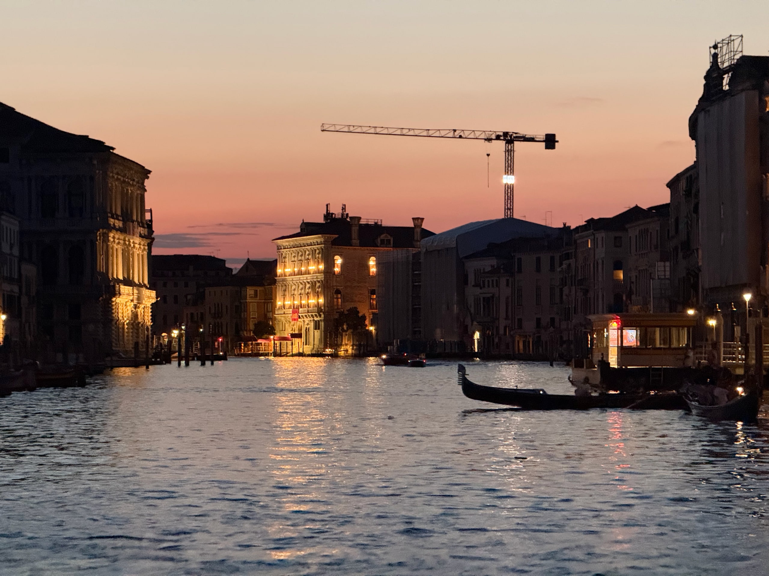 A vaporetto and gondola moving along a canal beneath a pink evening sky.