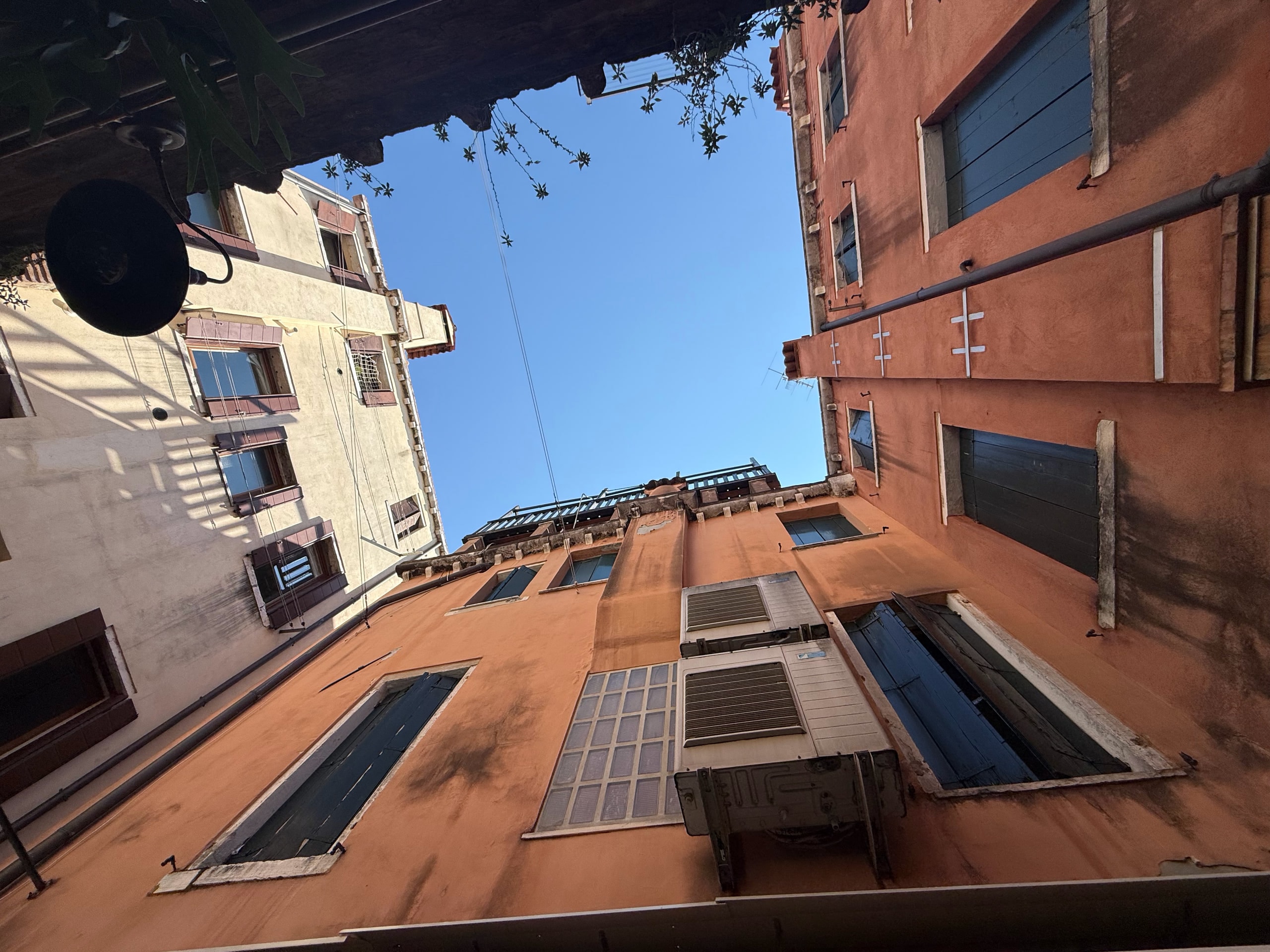 Looking upward between ochre and white facades in a narrow Venetian street.