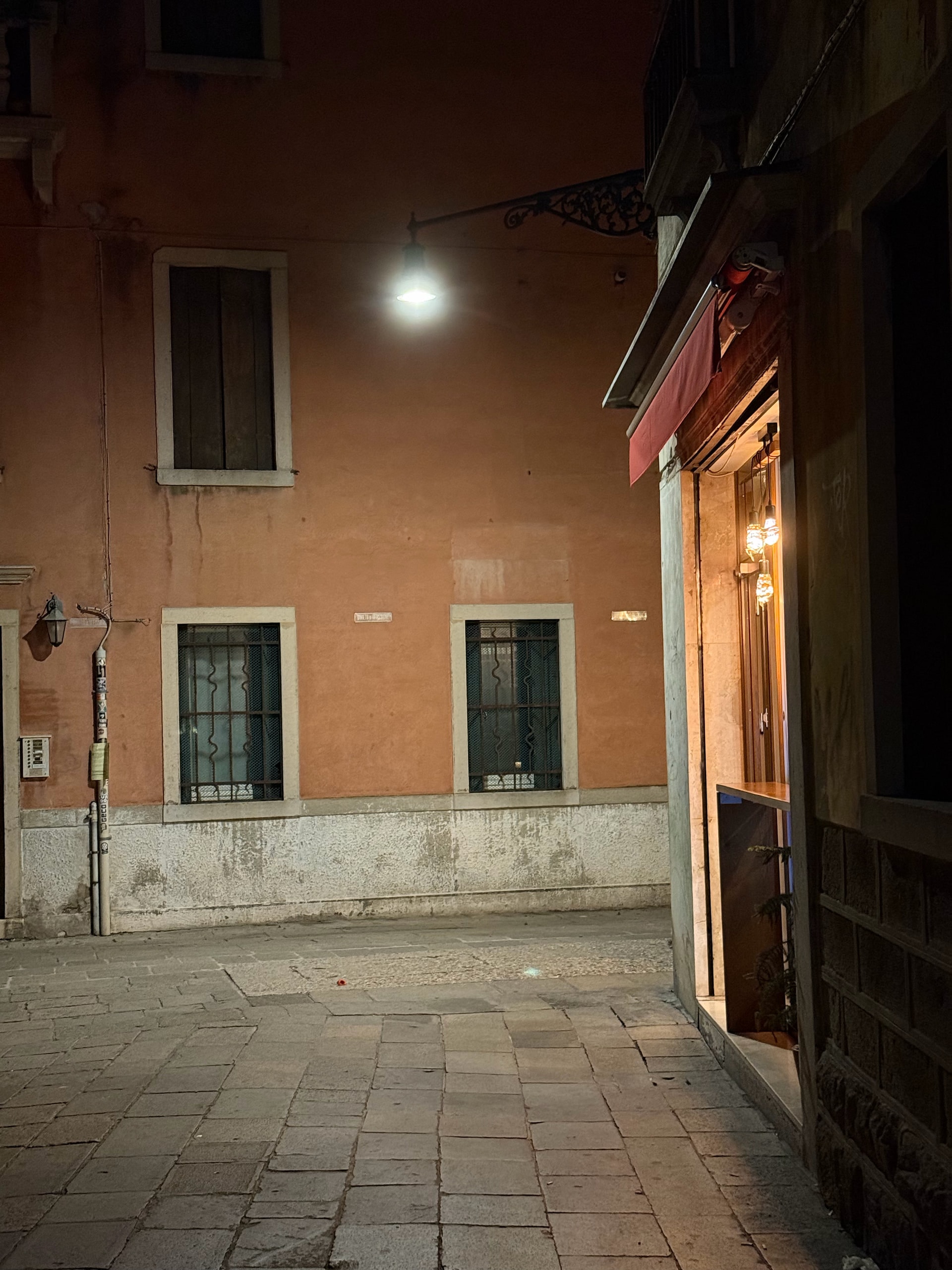 A narrow Venetian passage opening onto a warm facade beneath a street lamp.