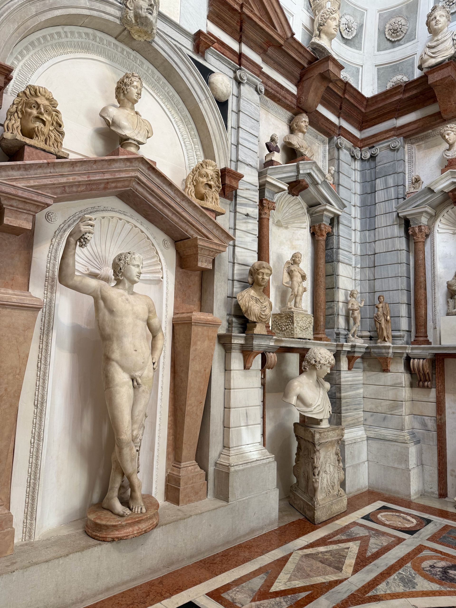 A marble sculpture court with classical figures and painted architectural panels.