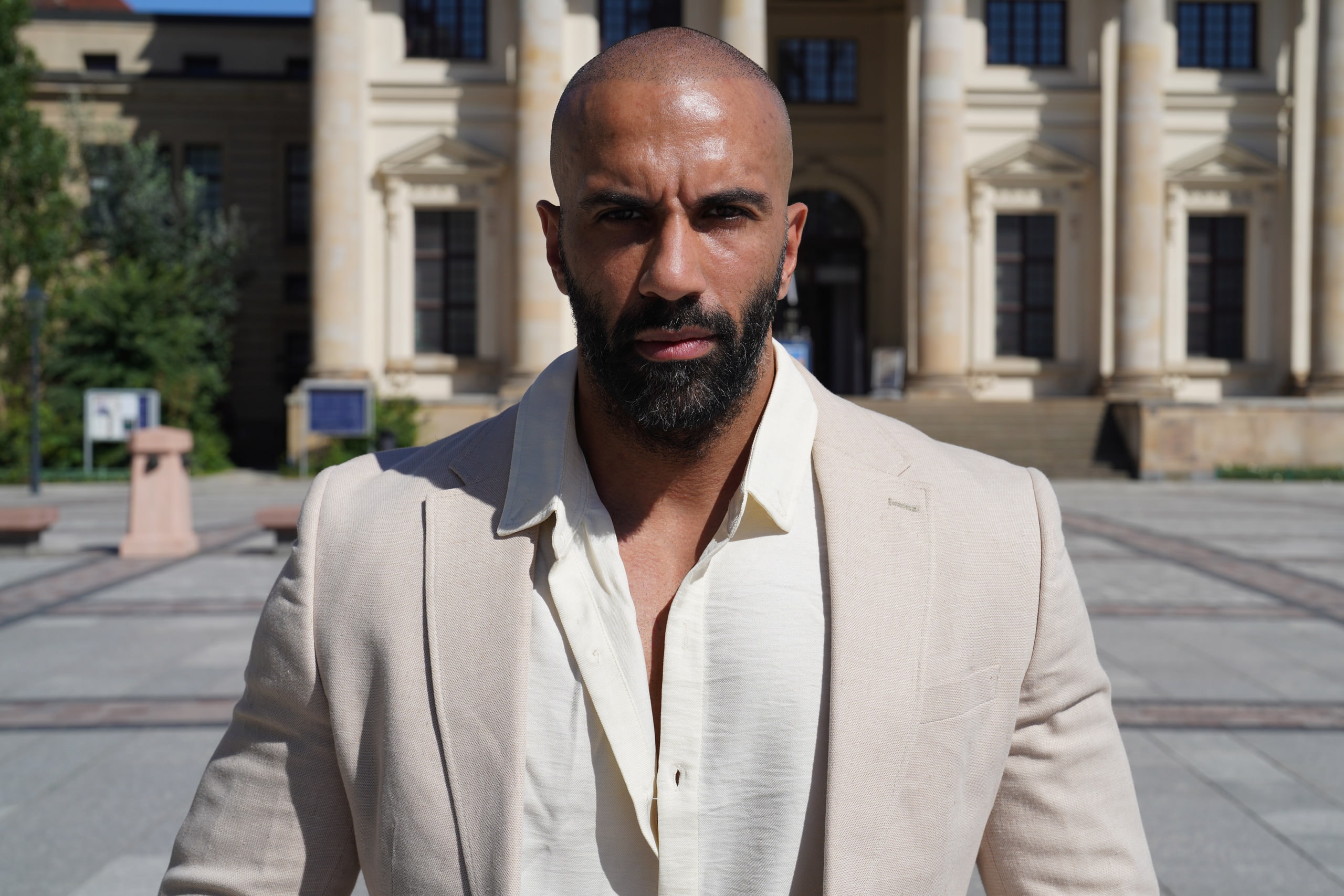 Close portrait of Amer El-Erwadi in a cream jacket, direct gaze, colonnade softened behind him.