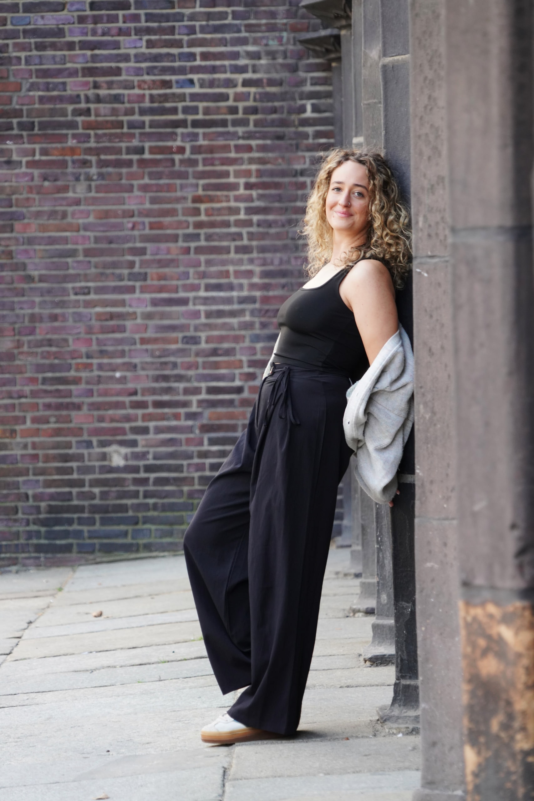 Larissa Kählert leaning against a brick pillar, her grey cardigan draped around her arms.