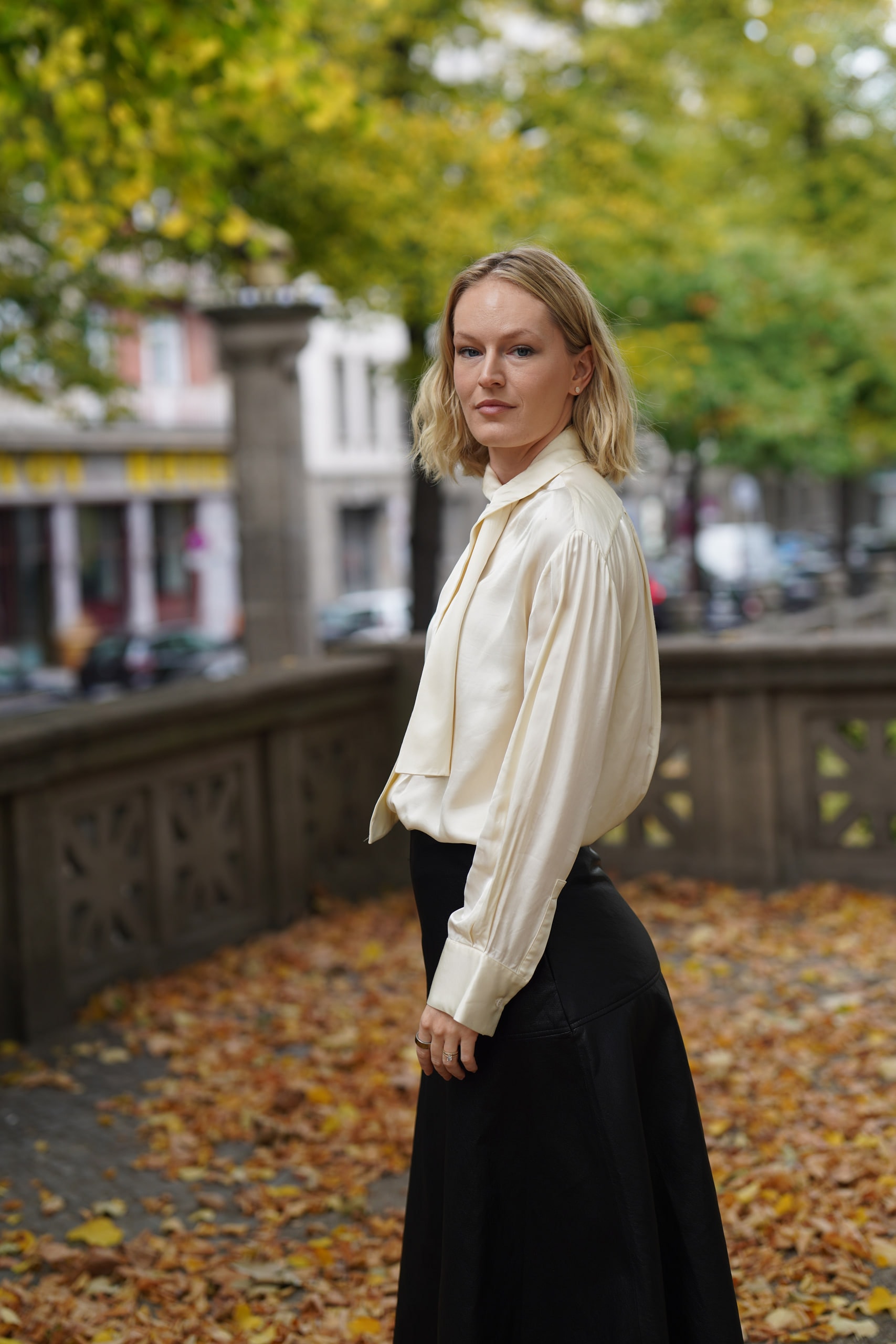 Sophia Repp looking back toward the camera beside a stone balustrade beneath autumn trees in Berlin.