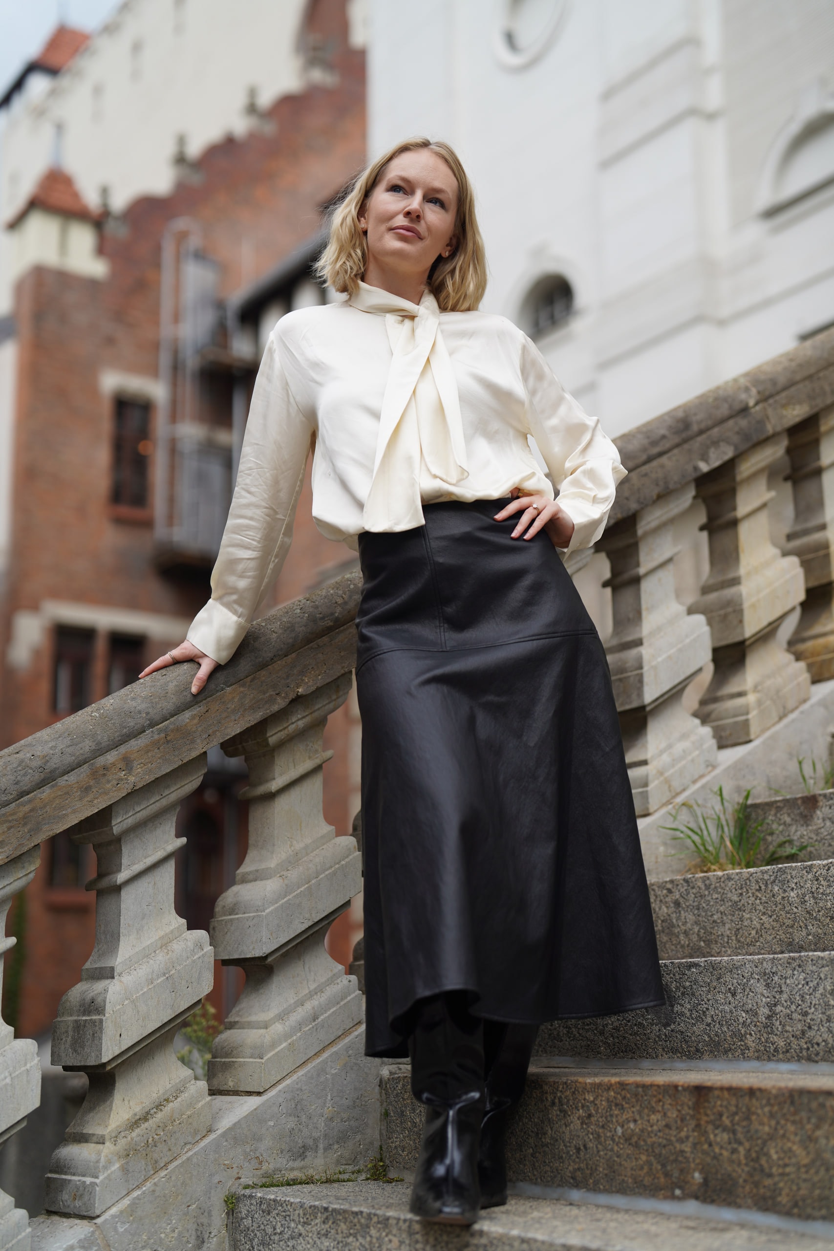 Sophia Repp standing on stone steps in a cream blouse and black skirt, one hand on the balustrade.